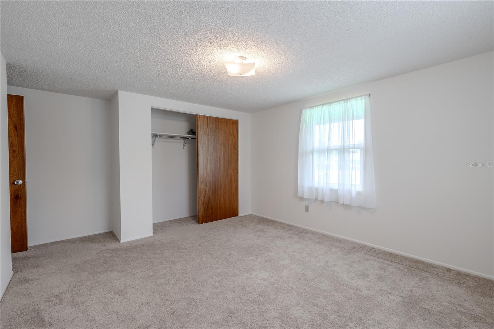 Bedroom #3 is generously sized and offers plenty of natural light from dual windows, creating a warm and airy feel. The neutral walls and carpeting provide a comfortable backdrop for a variety of uses—from a restful guest room to a productive home office or hobby space. A standard closet with sliding wood doors offers practical storage, while the room’s simple layout makes furnishing and decorating effortless. This flexible space is ready to adapt to your needs.