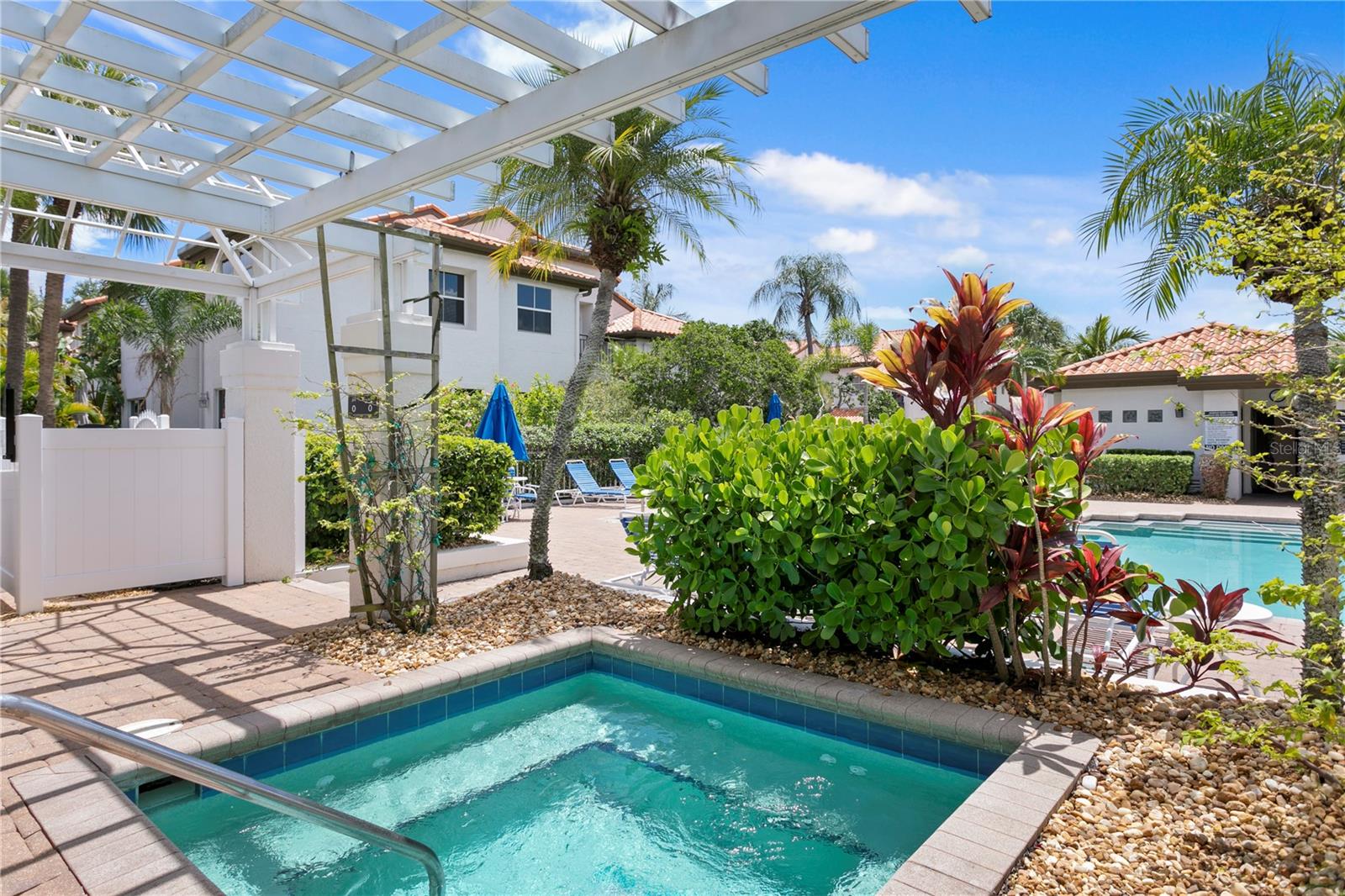 The hot tub is nestled under a charming pergola, surrounded by lush tropical landscaping.