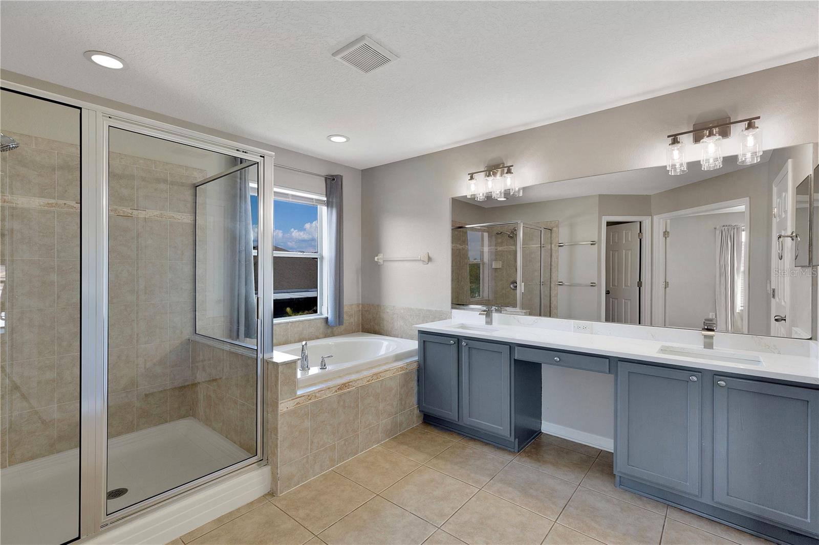 Double vanity, linen closet, soaking tub, and Quartz countertops with tiled shower wall.