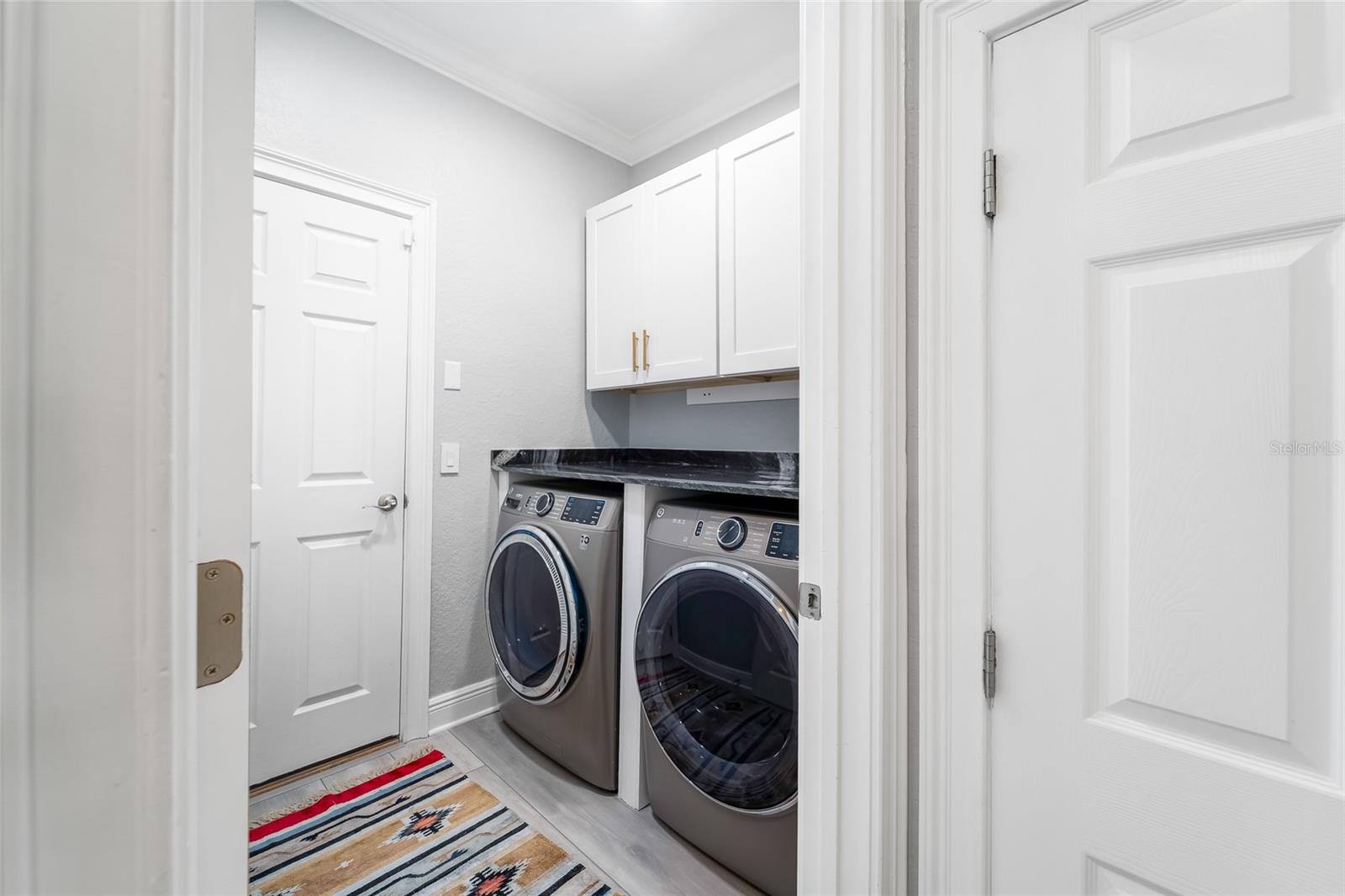 Indoor laundry with top end washer/dryer, marble countertop and custom cabinets.
