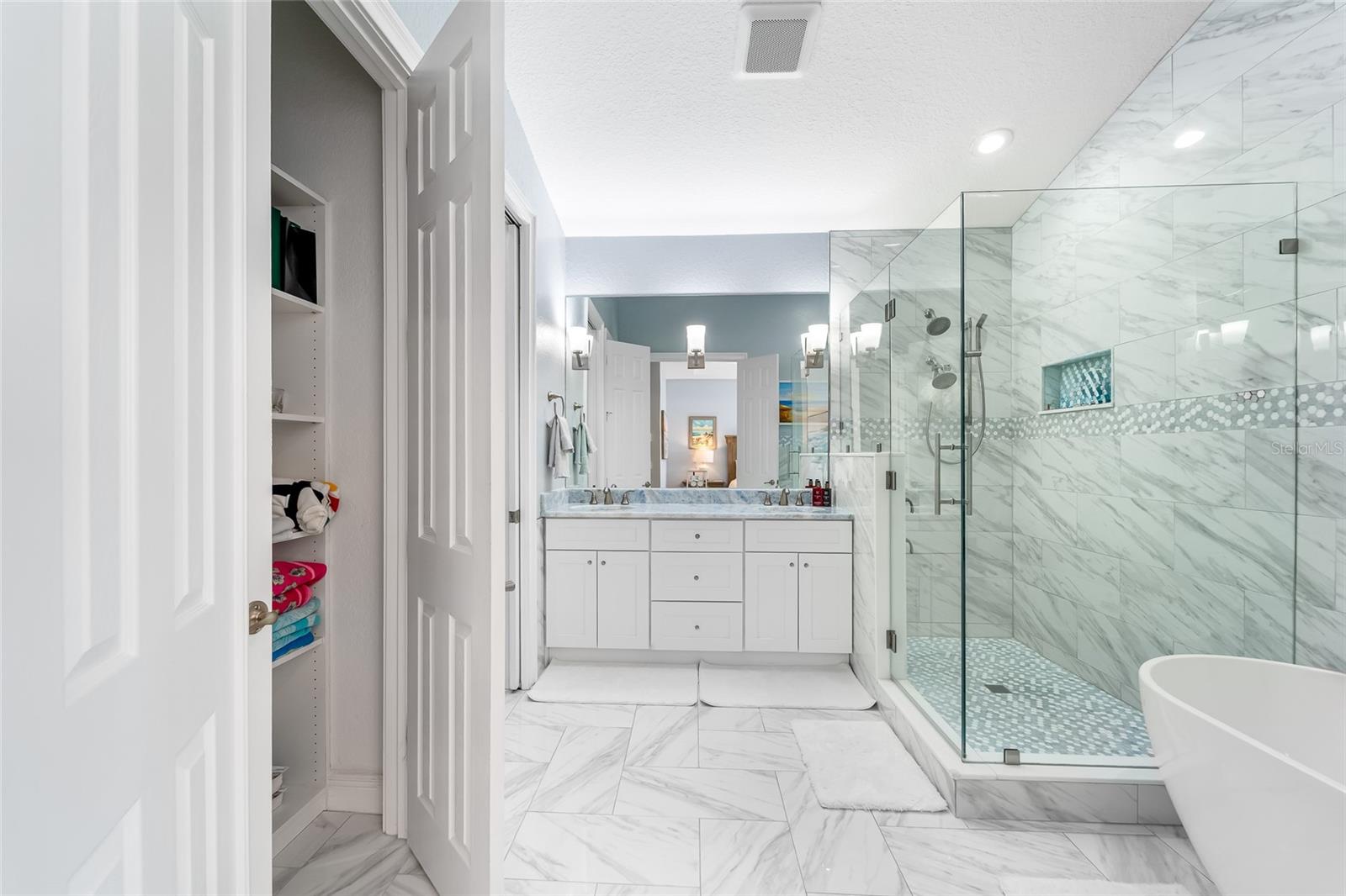 Primary bathroom with laundry closet, beautiful floors and frameless glass, double head shower.