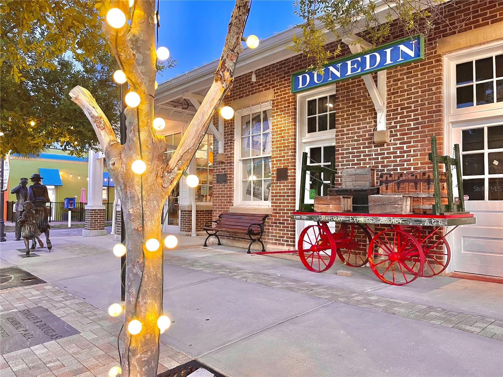 Light on at the baggage cart near statues on Main St in front of the Dunedin History Museum.