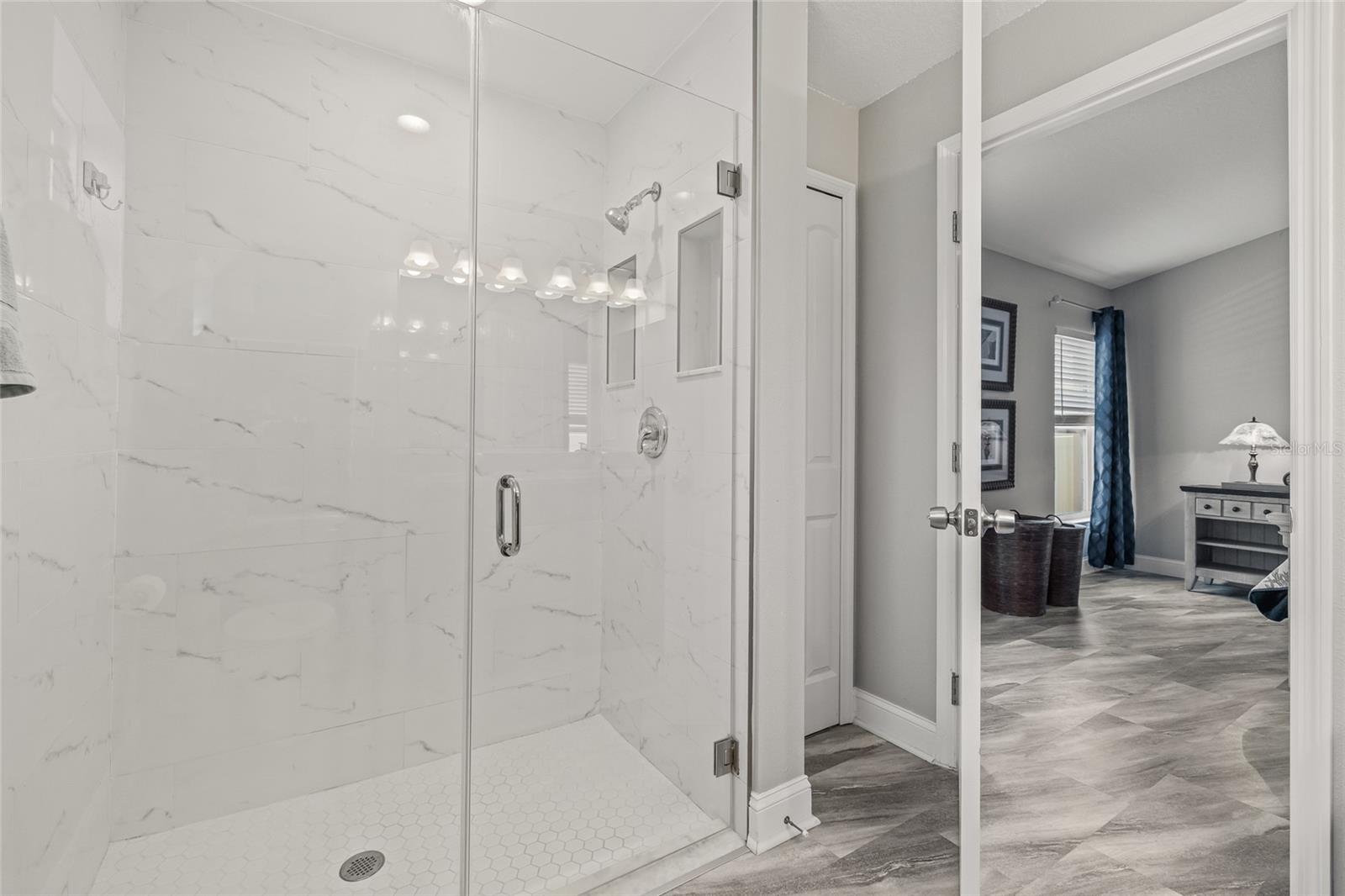 Step into your serene retreat with this spa-inspired bathroom showcasing a luxurious glass-enclosed shower, marble-style tile, and double niches for convenience.