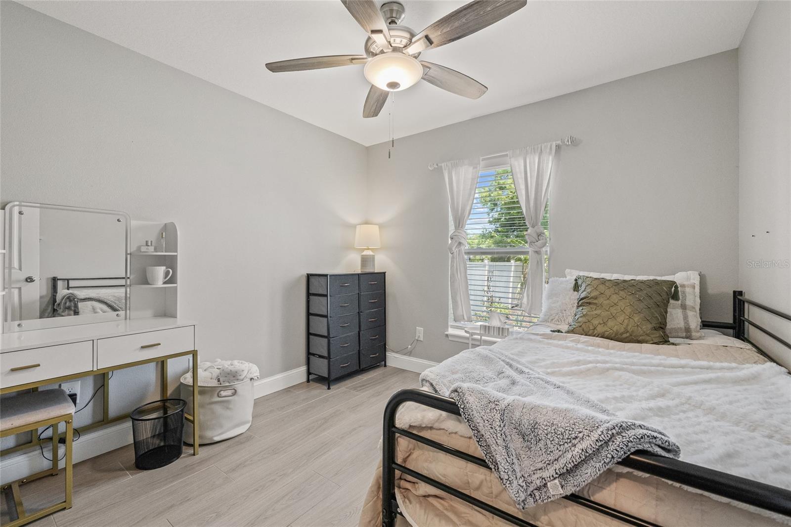 A cozy, bright bedroom with soft tones, modern ceiling fan, and natural light filtering through the window. Perfect for guests, kids, or a tranquil home office.