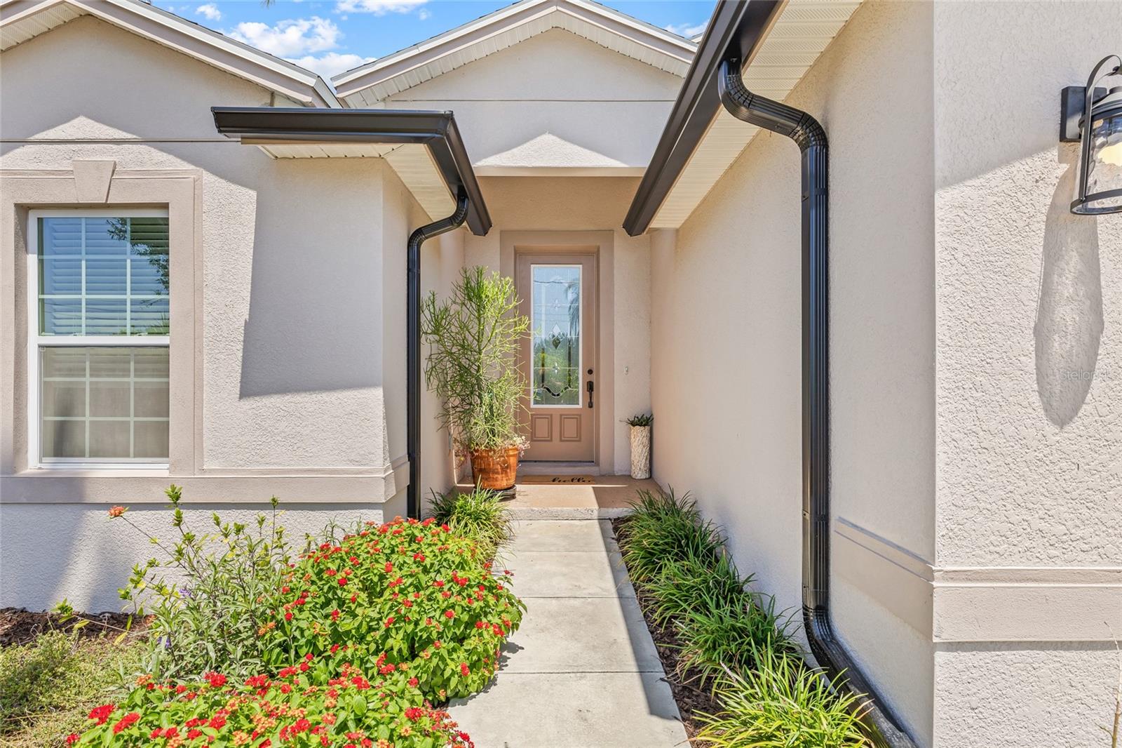The front exterior of the home welcomes you with tropical landscaping, new gutters, and a two-car garage, all framed under a clear Florida sky.