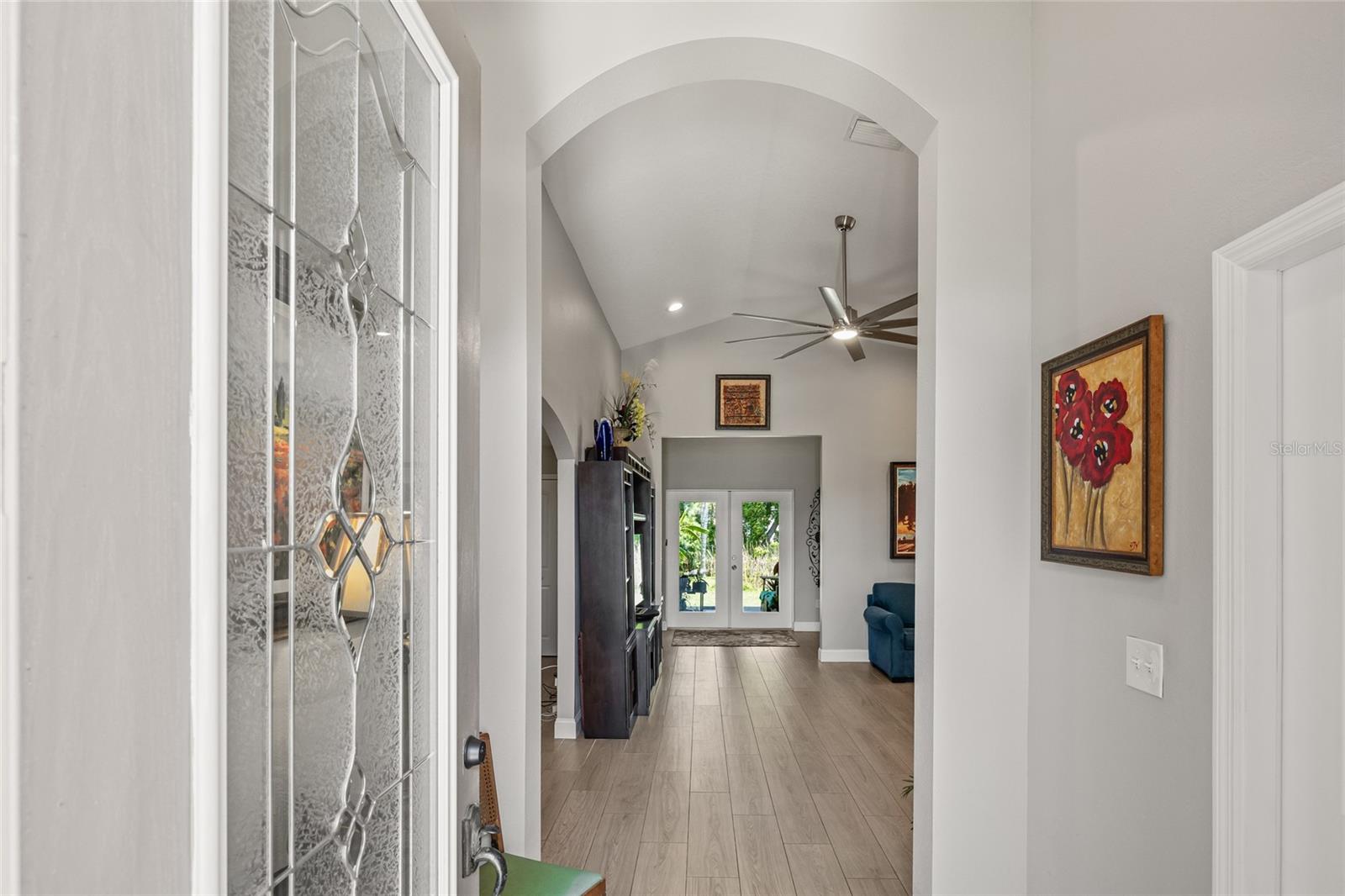 Step through a decorative glass front door into a space filled with light, high ceilings, and an elegant archway framing your view straight to the backyard.
