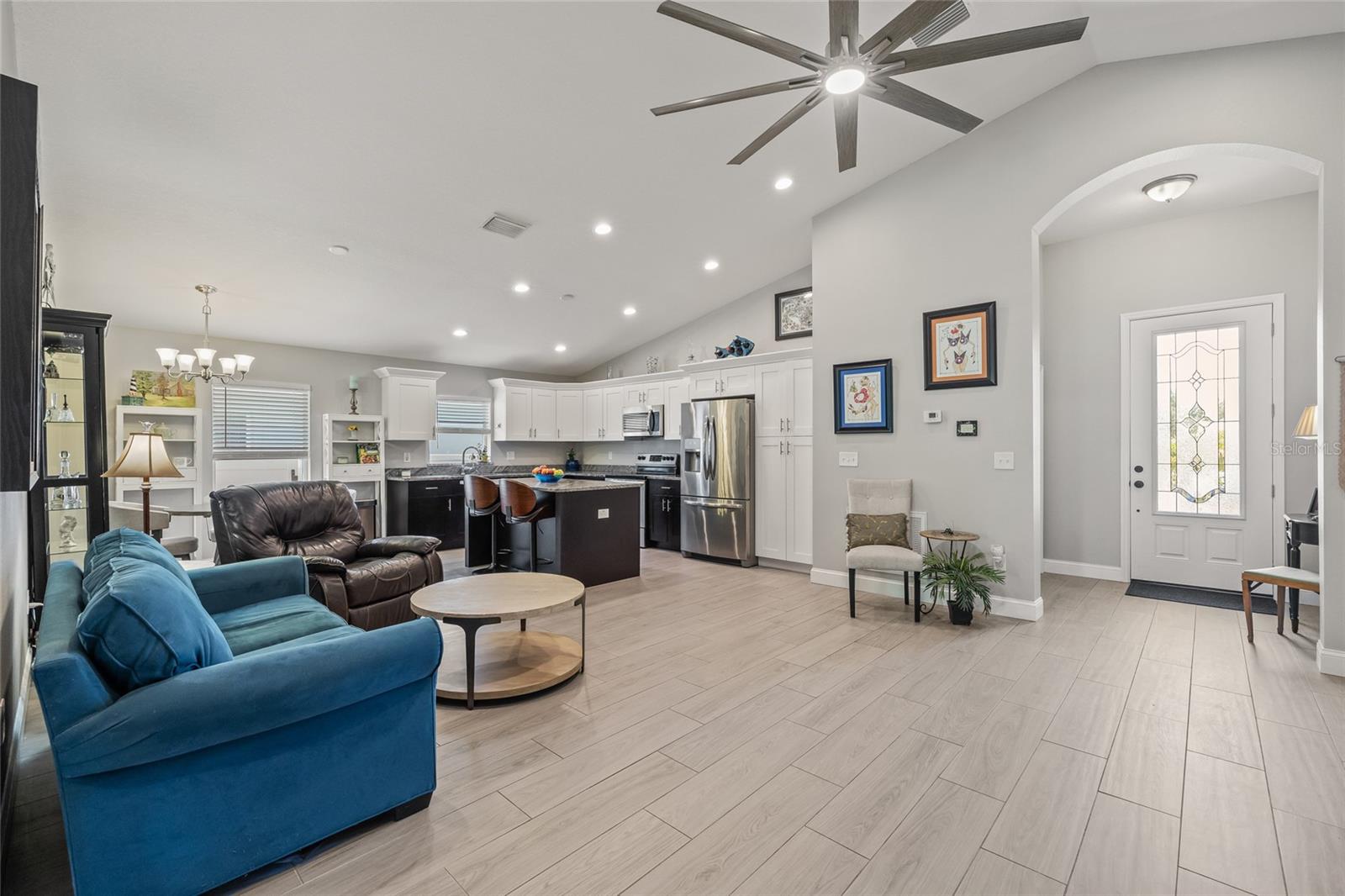This bright and airy living room features vaulted ceilings, a large designer ceiling fan, and seamless flow into the dining and kitchen areas—perfect for hosting or relaxing.