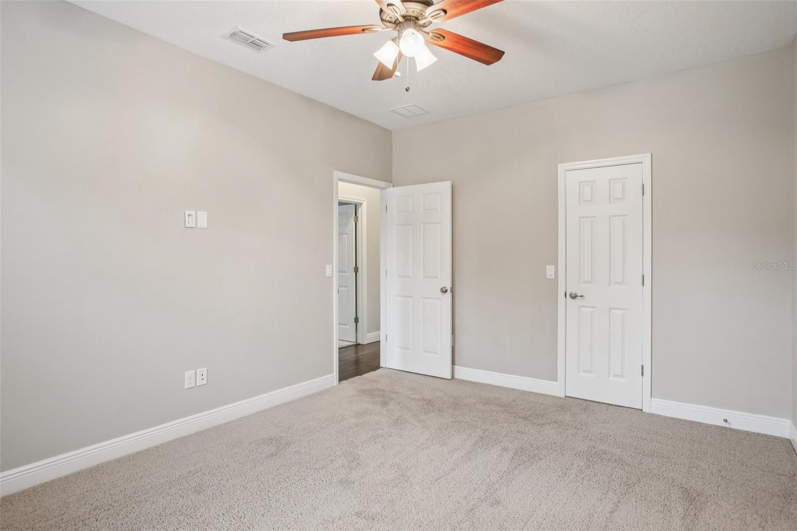 Spacious bedroom with neutral tones and ceiling fan.