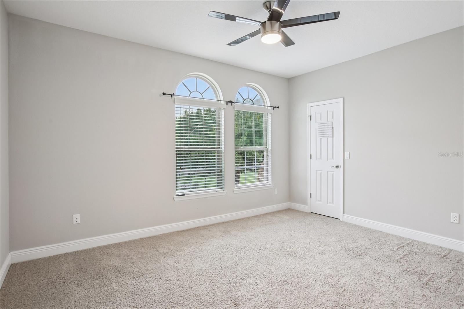 Bright bedroom with arched windows and modern ceiling fan.