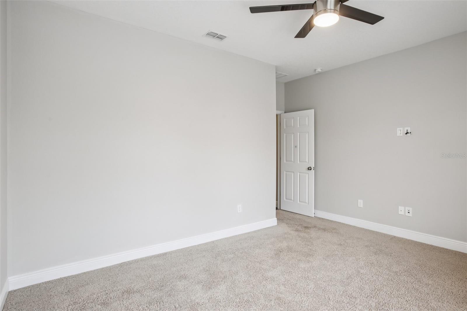 Neutral-toned bedroom with modern ceiling fan and plush carpet.
