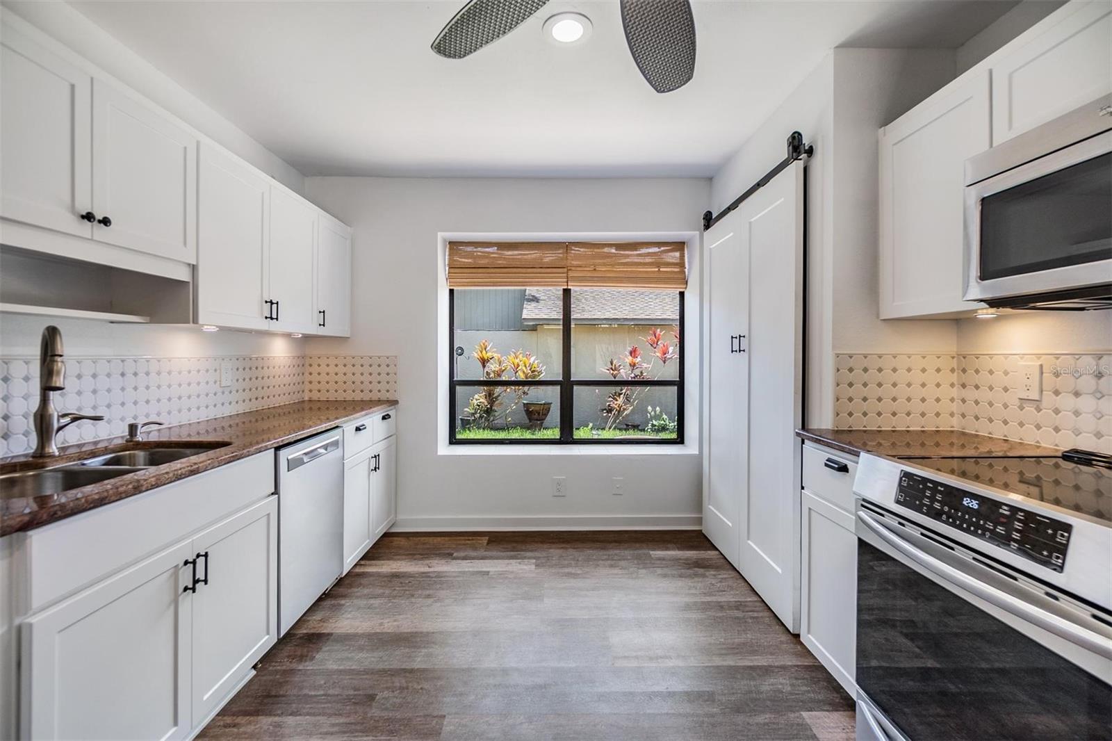 Updated kitchen with all stainless steel appliances, granite countertops, bright white modern cabinets, a pantry, and passthrough window to the dining room.