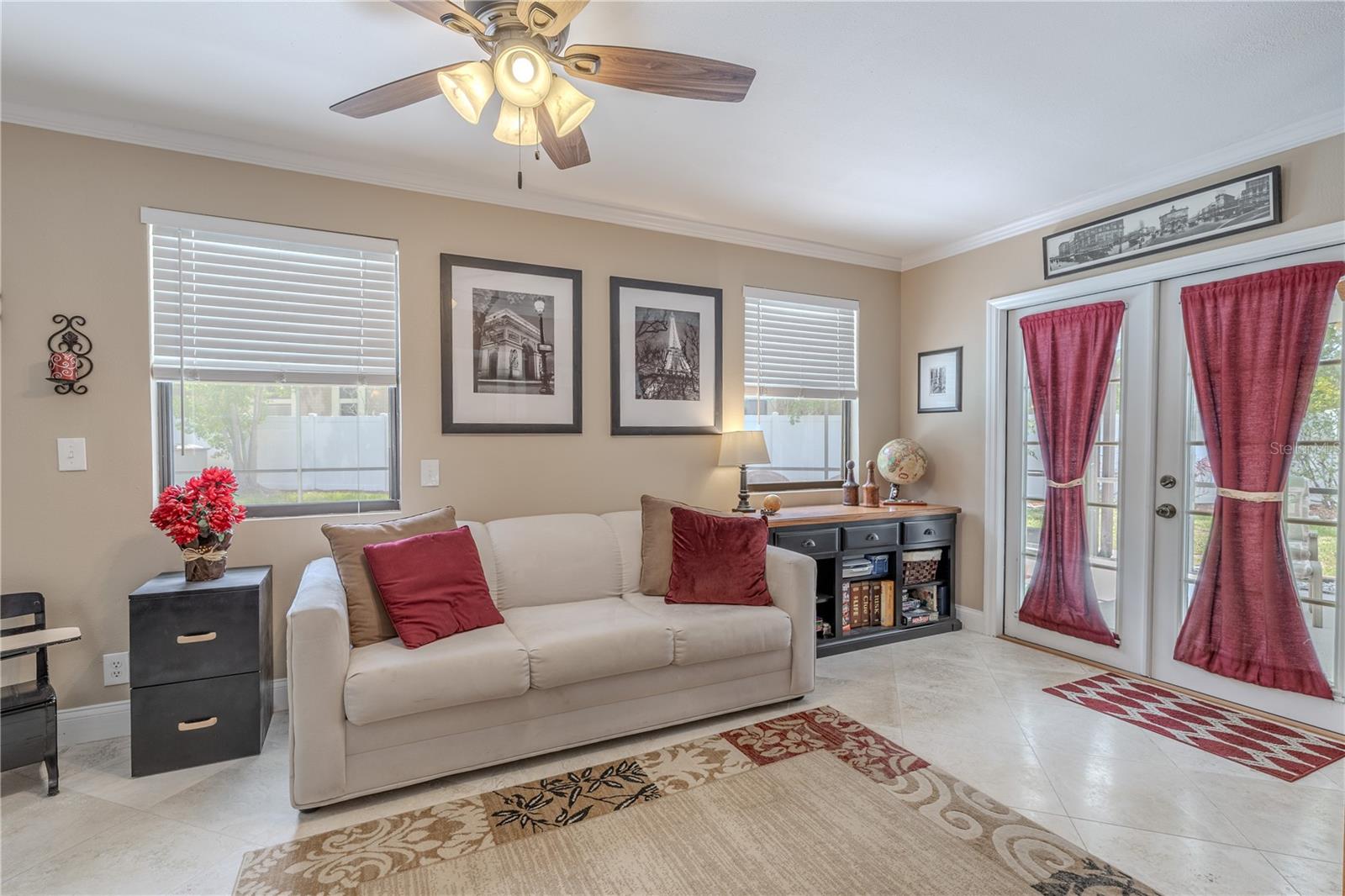 The home's Florida room offers a flexible and light-filled bonus space ideal for a home office, reading lounge, creative studio, or den. Enclosed by glass French doors, this inviting room features neutral tile flooring, crown molding, and a ceiling fan for added comfort.