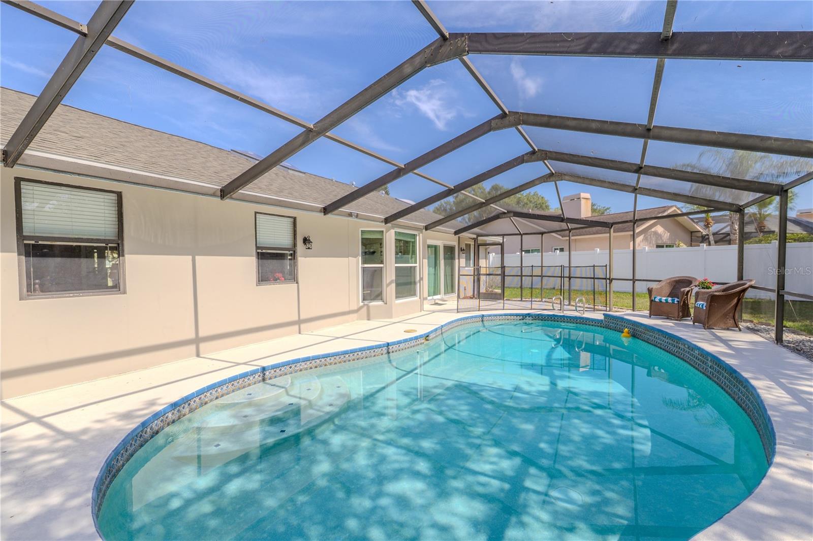 The pool features a gently sloped entry,  and tile accents along the waterline add a stylish touch, while the expansive pool deck offers plenty of room for outdoor furniture, grilling, and entertaining.Fully screened for protection from the elements while still letting in the warm Florida sunshine. The covered patio area is equipped with ceiling fans and multiple access points from the home,  a shaded retreat with views of the privacy-fenced backyard.