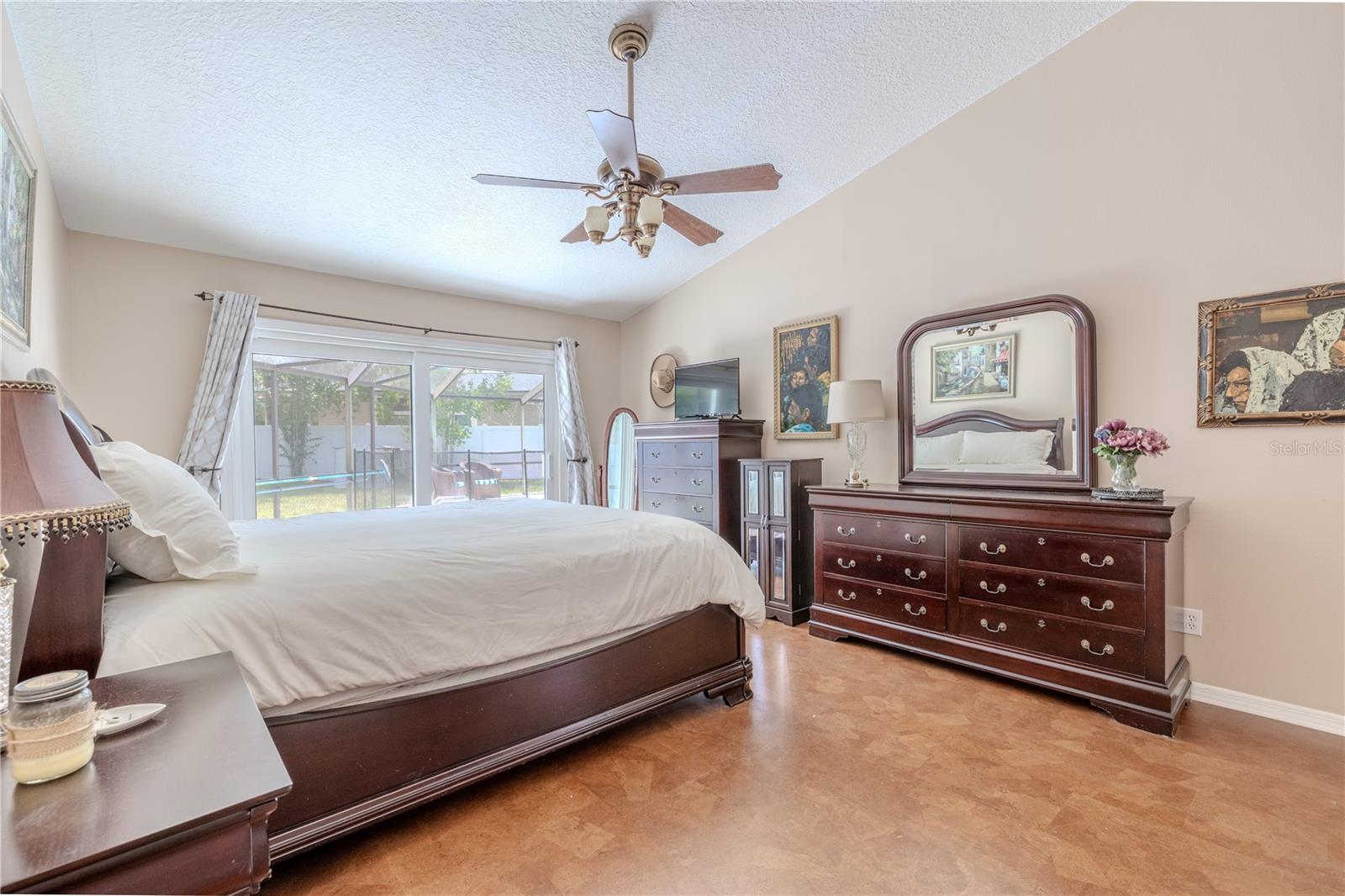 The spacious primary bedroom offers a peaceful retreat with serene views of the backyard and pool through a large sliding glass door that fills the room with natural light. Neutral walls and easy-care wood-look flooring create a warm, inviting atmosphere that complements any style.