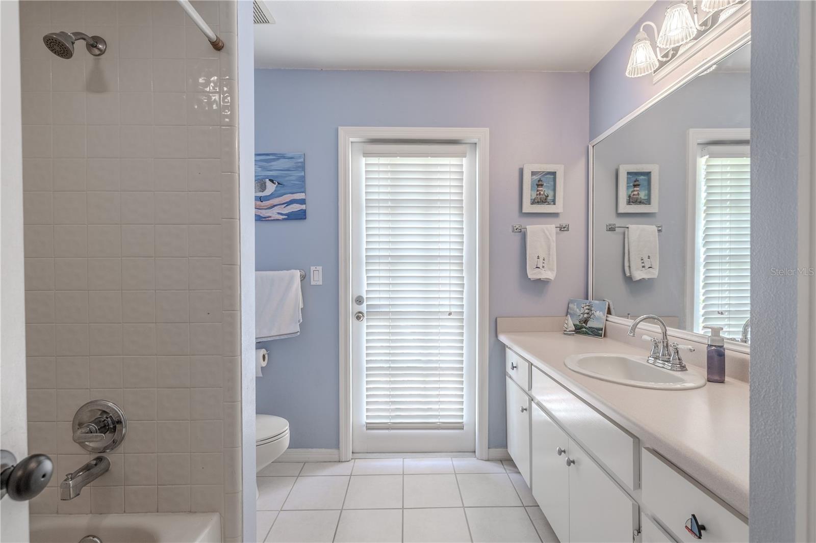 The second full bathroom features a bright and cheerful design with coastal-inspired colors and finishes. A full-size shower and tub combo offers flexibility for guests or family, while the extended vanity with ample counter space and storage makes daily routines a breeze. A large wall-mounted mirror and updated light fixture add both function and charm.This bathroom also includes direct access to the backyard and pool area, making it an ideal cabana-style bath for rinsing off after a swim or enjoying seamless indoor-outdoor living. With tile floors for easy maintenance and a clean, airy vibe, this space is as practical as it is welcoming.