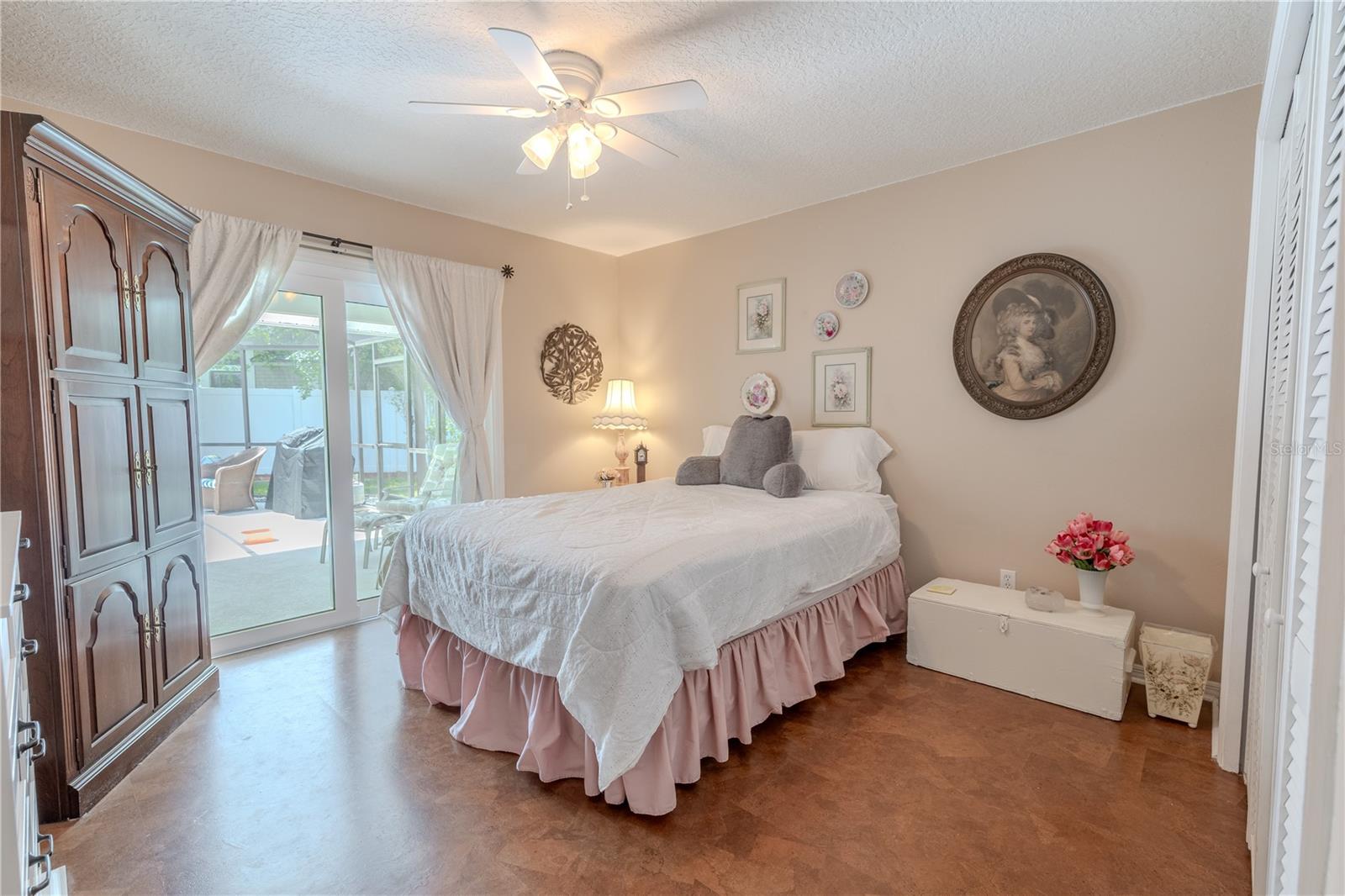 The third bedroom has  direct access to the screened lanai and pool area, Natural light fills the space through the glass doors, enhancing the warm neutral tones, cork flooring and creating a calm, inviting atmosphere.This room features generous closet space, ceiling fan, and low-maintenance flooring, making it ideal for guests, multi-generational living, or a private home office. With its own entry to the lanai, this bedroom provides flexibility and privacy, setting it apart as a truly special space in the home.