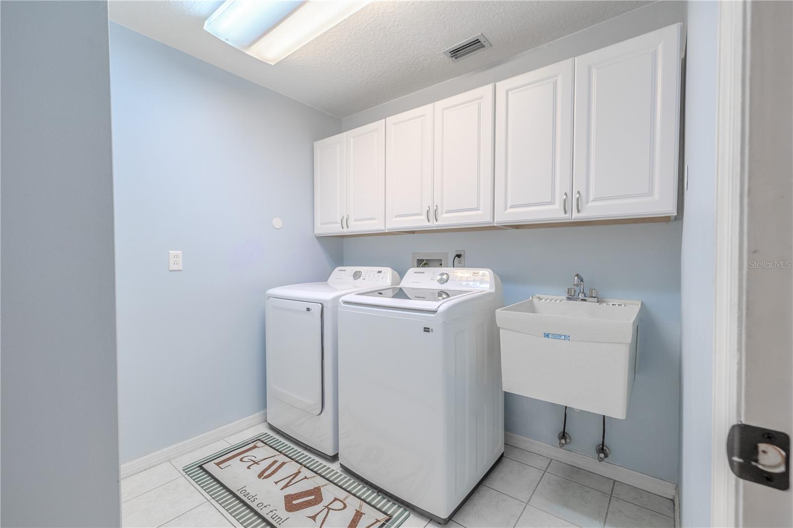 Crisp, clean, and practical, the dedicated laundry room offers everything you need to simplify daily routines. This bright space features a full-size washer and dryer set beneath a wall of white cabinetry that provides generous storage for linens, cleaning supplies, and essentials.