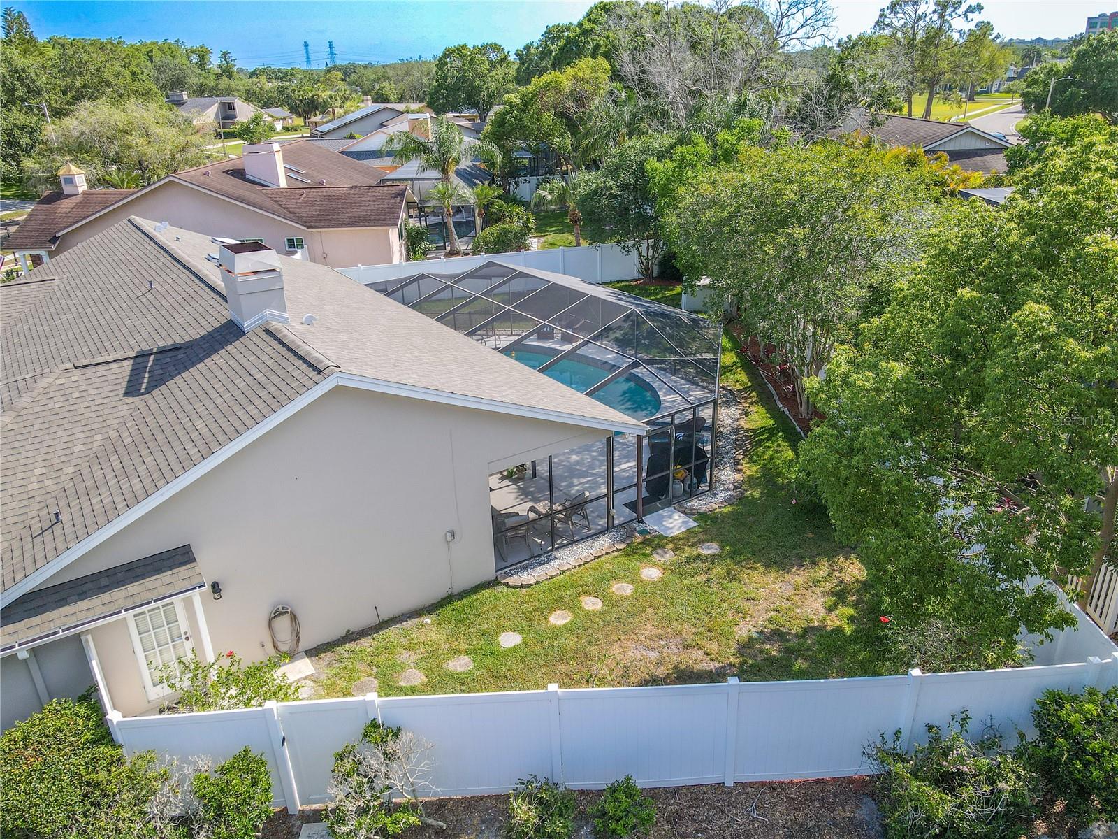 A green lawn and thoughtfully placed stepping stones lead to a garden bed lined with flowering shrubs and mature trees, adding beauty and a natural privacy buffer.
