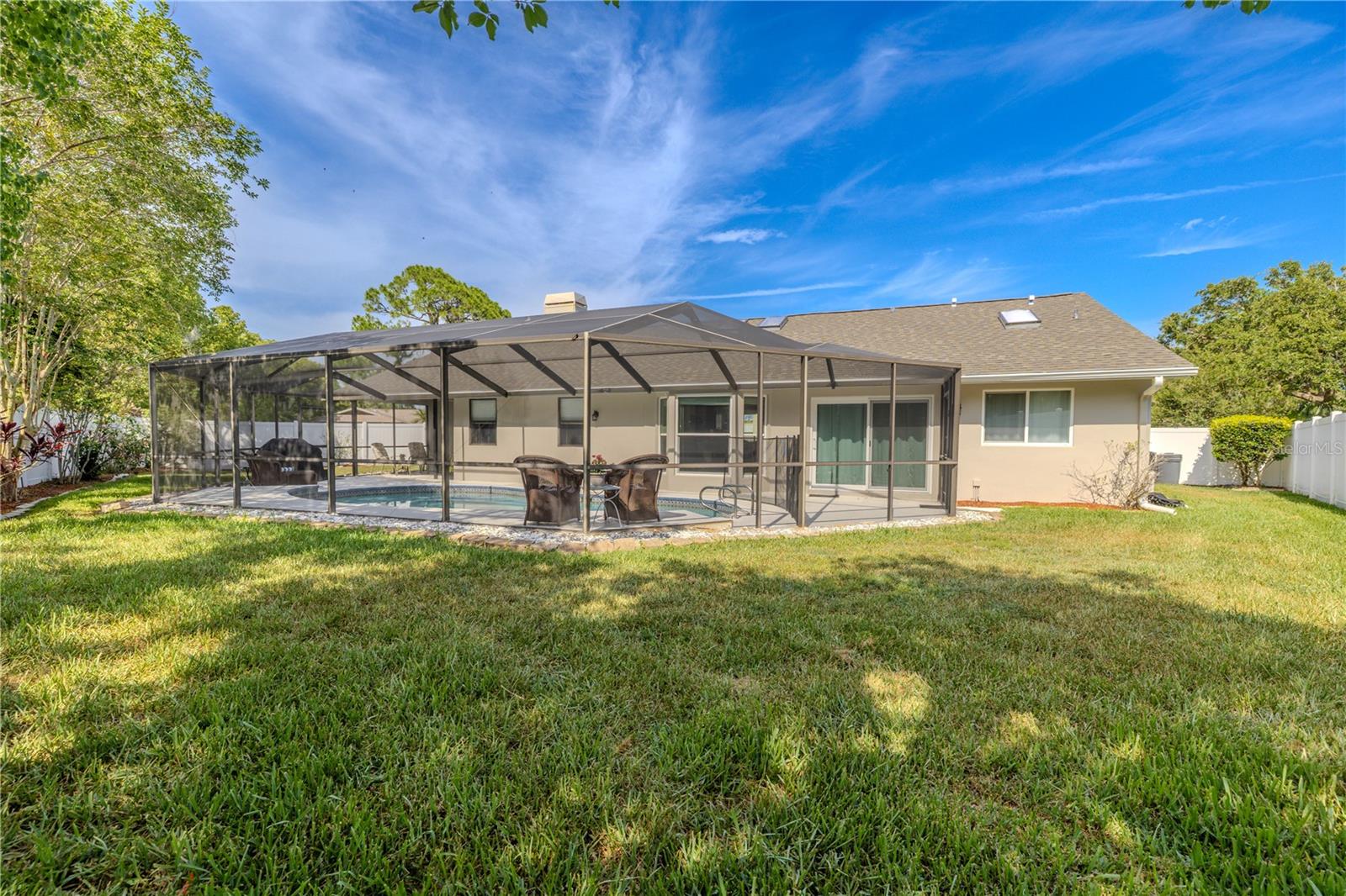 The backyard offers a peaceful and private oasis, fully enclosed by crisp white vinyl fencing. A screened-in lanai provides year-round enjoyment of the in-ground pool, complete with ample space for outdoor dining or lounging in the shade.