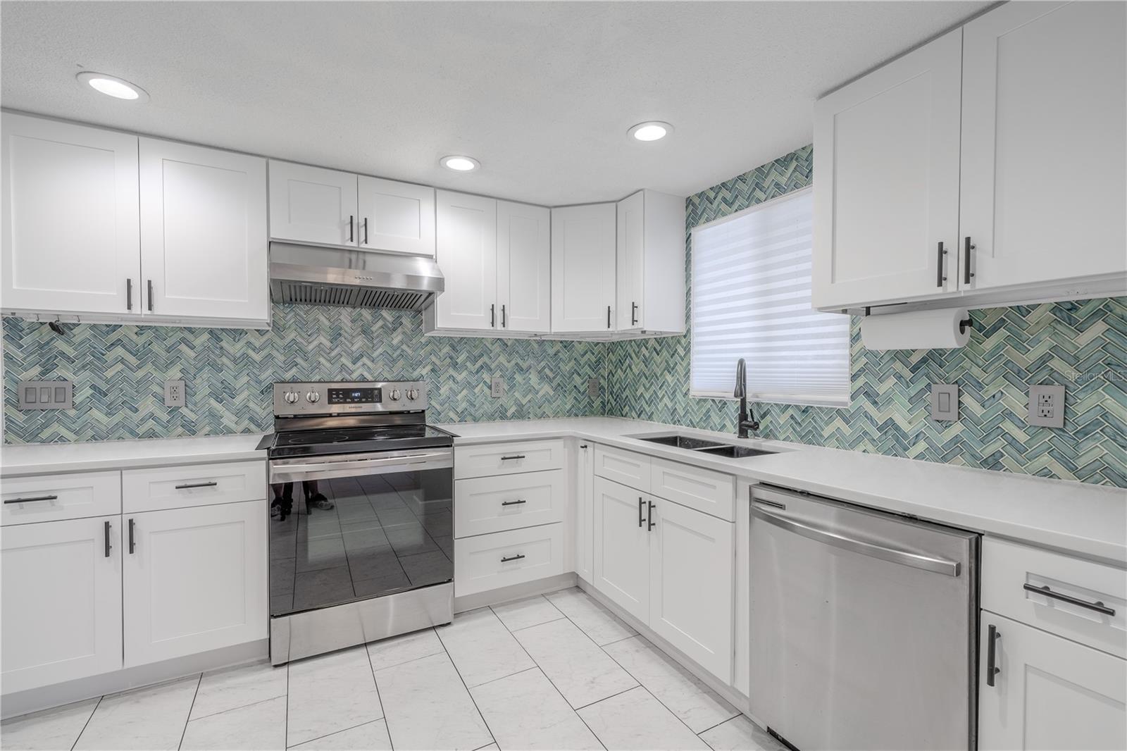 Recessed lighting and a central window over the sink keep the space bathed in natural and ambient light, while the soft neutral  tones and easy-care tile flooring tie everything together.