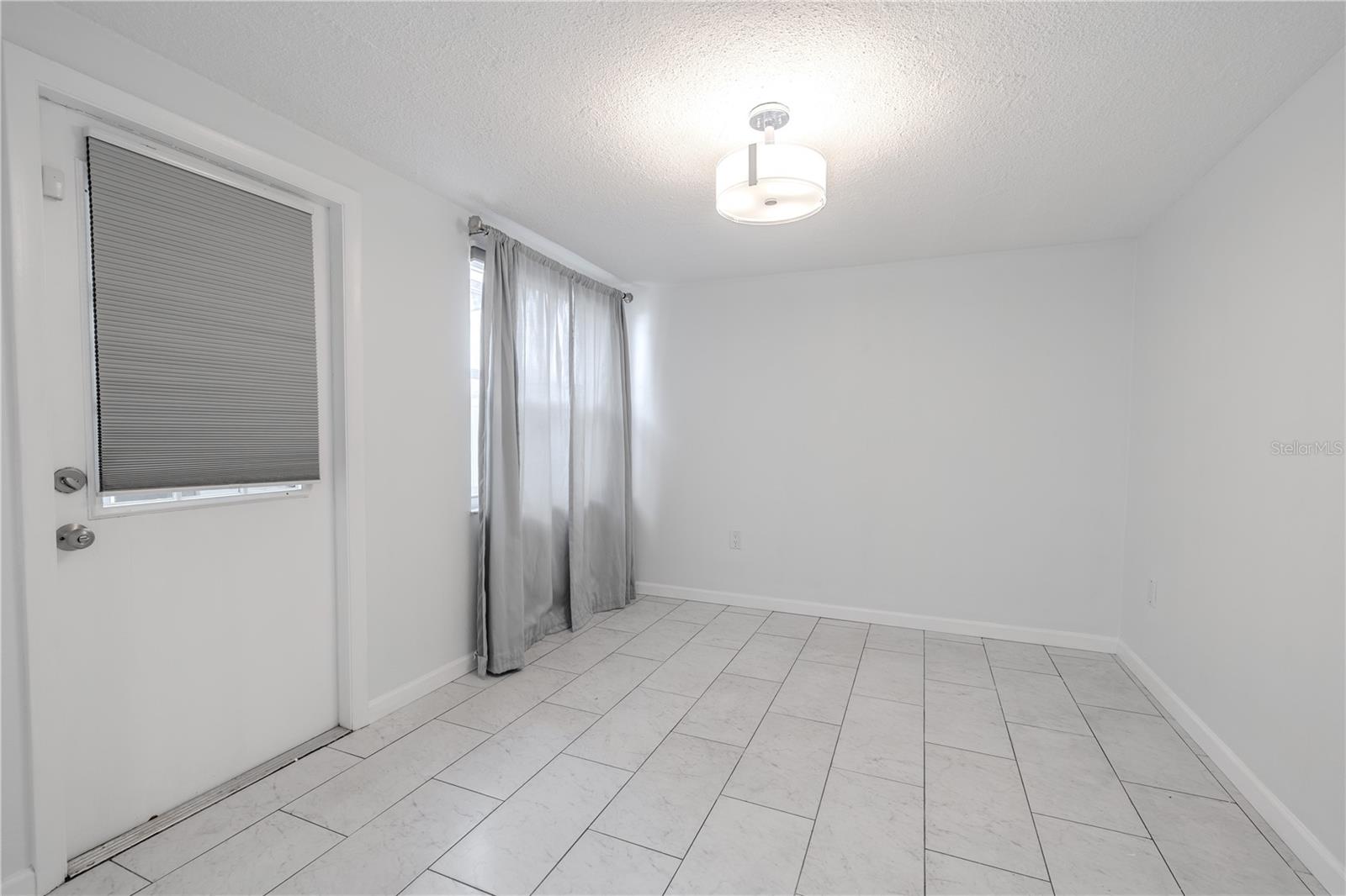 Large windows dressed in airy curtains provide a pleasant view of the backyard and screened-in patio, creating a lovely setting for both casual meals and more formal gatherings.