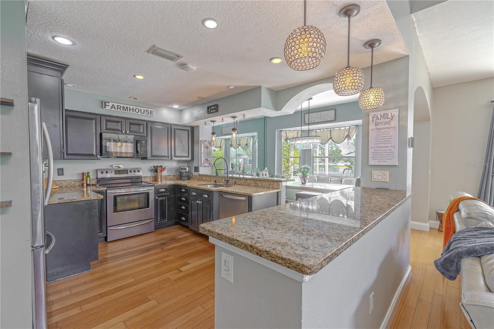 Recessed lighting and pendant fixtures provide both task lighting and ambiance, while arched architectural details and pass-through openings create seamless connection to the adjacent living and dining spaces.