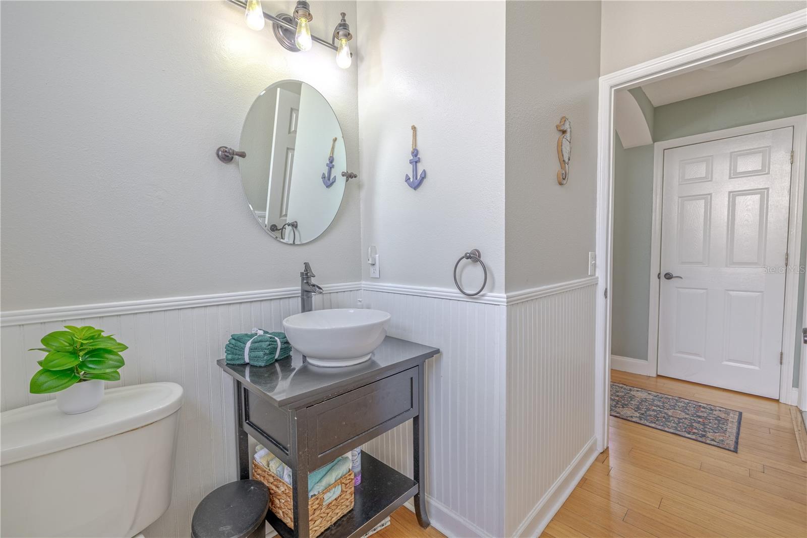 The downstairs half-bath is well-lit with a trio of exposed-bulb light fixtures and finished with bamboo flooring consistent with the rest of the main living area, this powder room is both practical and polished—a perfect blend of charm and convenience for guests.