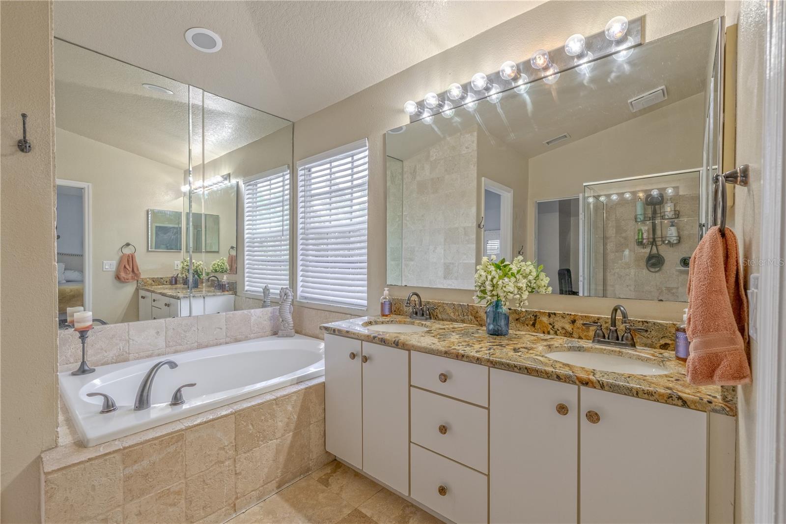 A deep soaking tub is set into a tiled surround with a mirrored wall above, adding a sense of depth and light to the space.