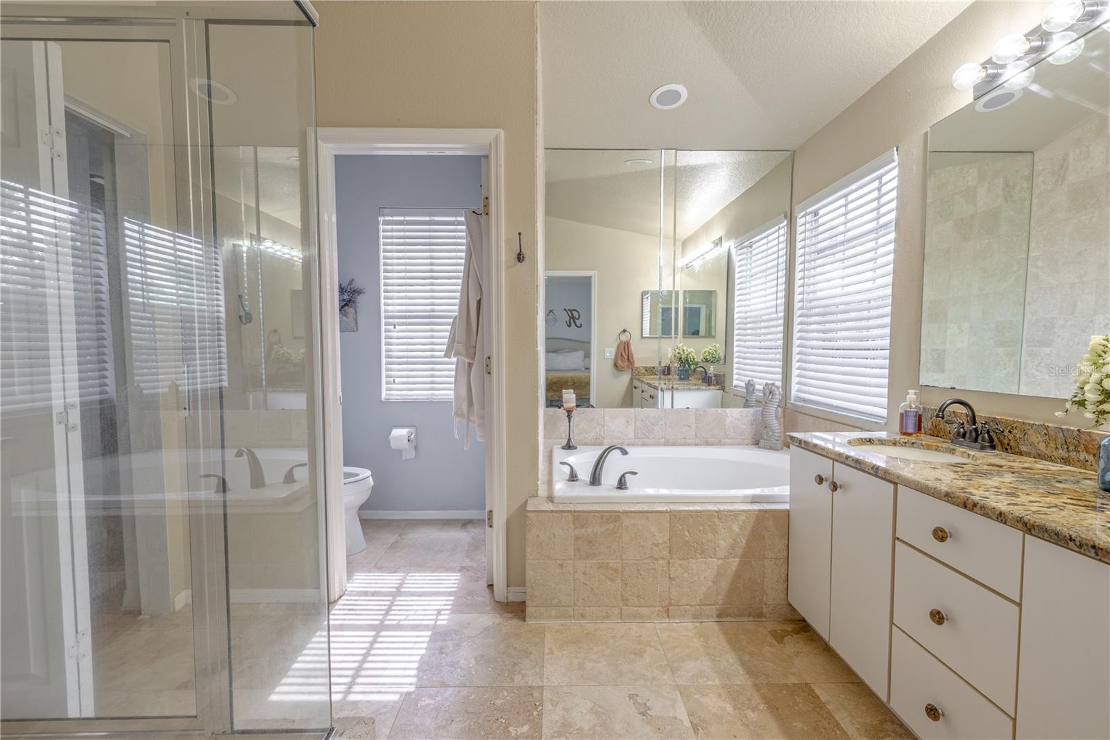 The spacious primary en-suite primary bath offers a serene, spa-like atmosphere with natural stone finishes and a thoughtfully designed layout. Finished with warm tile flooring that complements the bath’s natural tones, this primary suite bathroom delivers everyday luxury and comfort.