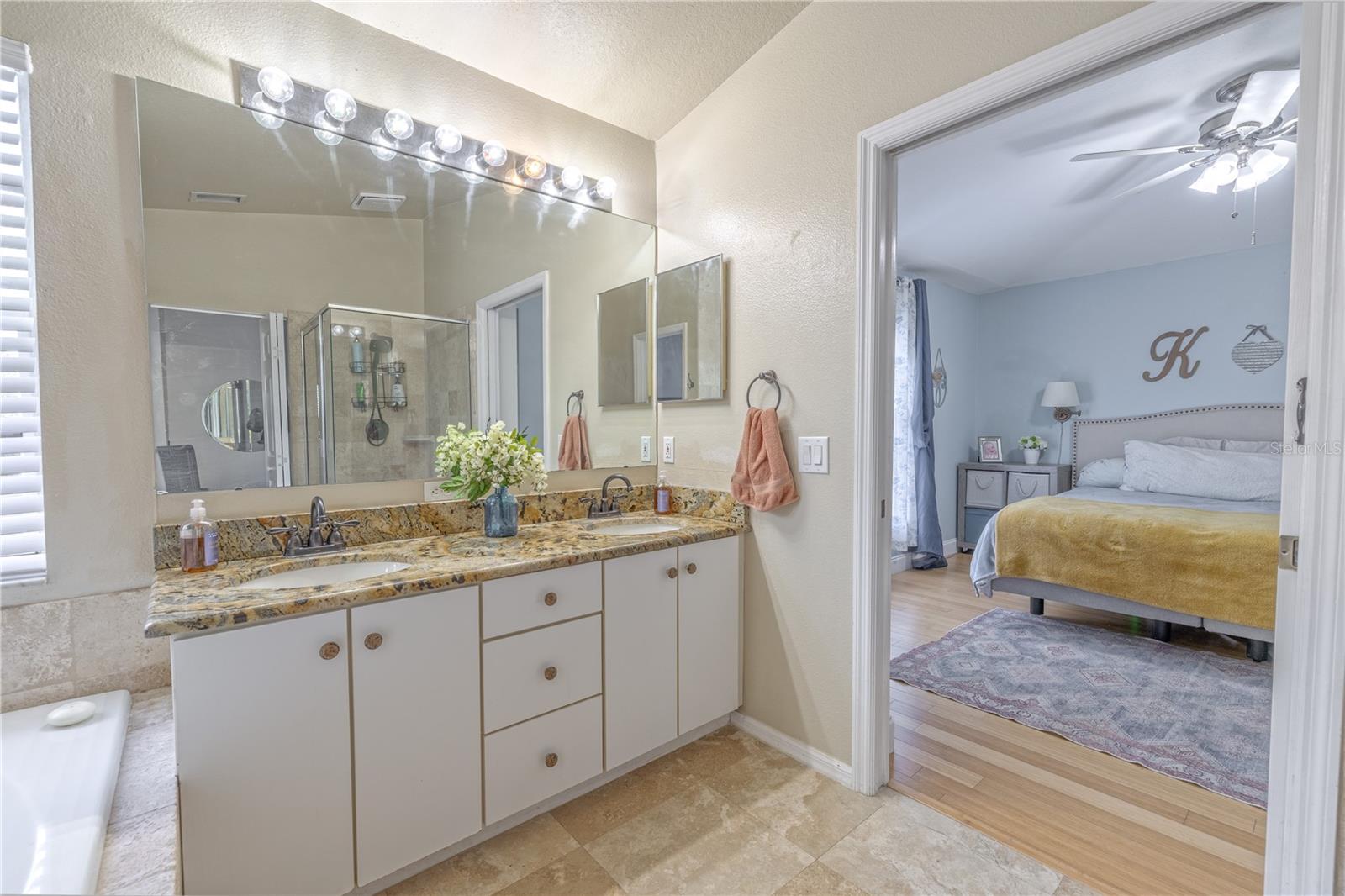 A large dual-sink vanity features granite countertops, under-mount sinks, and ample cabinet storage, set beneath an oversized mirror with updated vanity lighting.