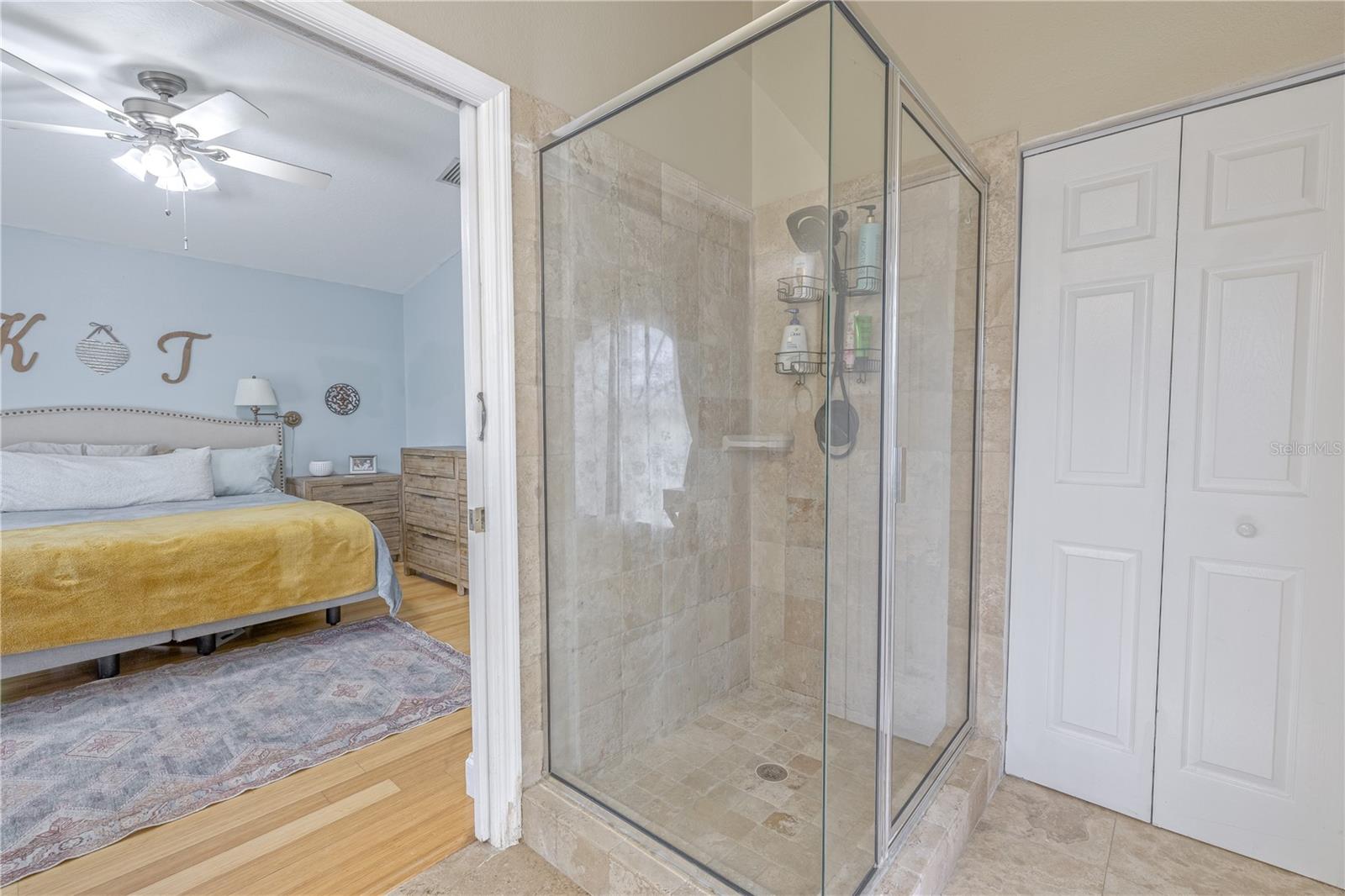 The walk-in shower is enclosed in clear glass and finished in neutral tile, creating a clean, timeless look. A private water closet adds function and privacy, while multiple windows with blinds provide soft, natural light throughout the day.