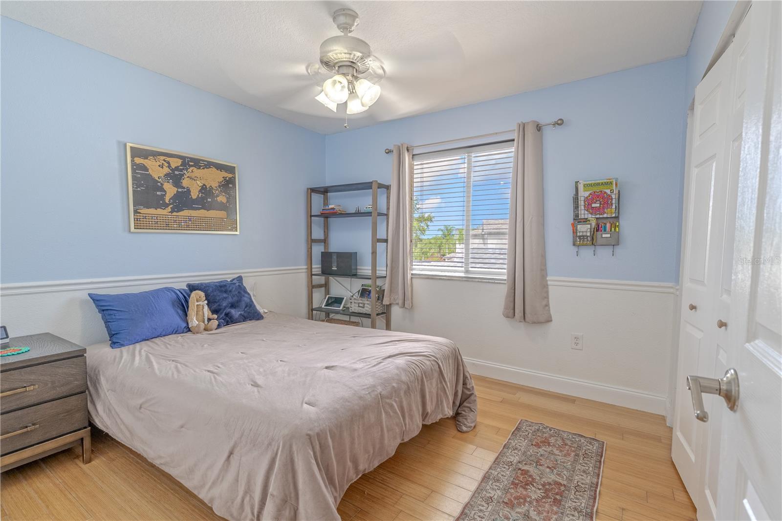 The second bedroom offers a bright and inviting space with crisp architectural details and a flexible layout to suit a variety of needs—whether used as a guest room, home office, or personal retreat. A large window fills the room with natural light, while the two-tone wall treatment with chair rail adds a subtle decorative touch.Bamboo flooring flows underfoot, echoing the warm tones found throughout the home. The ceiling fan provides added comfort, and a double-door closet offers ample storage. This thoughtfully designed room combines comfort and functionality in a tranquil, light-filled setting.
