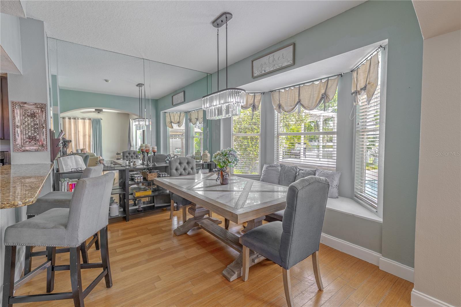 Bamboo flooring flows seamlessly from the adjacent living space, creating warmth and continuity.A mirrored accent wall enhances the sense of space and brightness, while a modern, dual-pendant chandelier adds an upscale design touch.