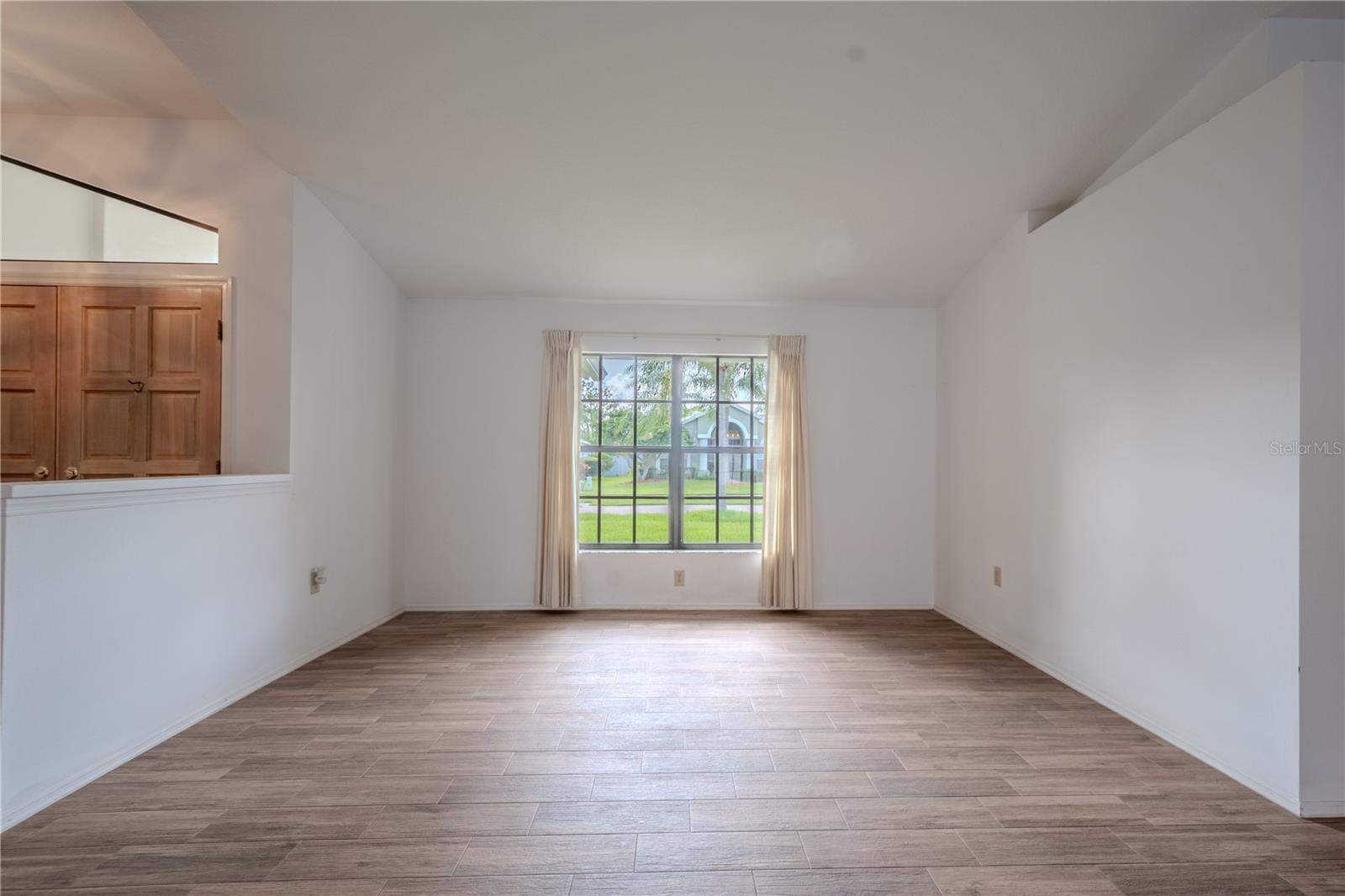 Just off the foyer, the living room welcomes you with soft natural light streaming through a wide picture window, offering peaceful views of the front lawn and palm-lined street beyond.