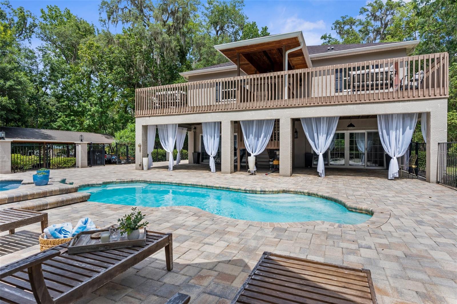 Heated pool and jacuzzi with paver deck and iron fence.