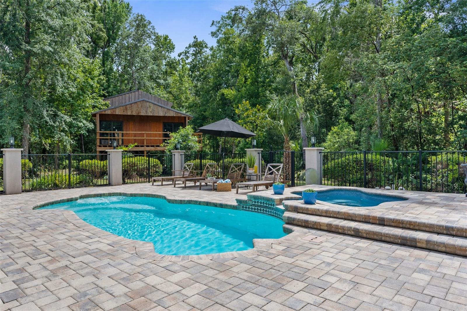 Heated pool and jacuzzi with paver deck and iron fence.