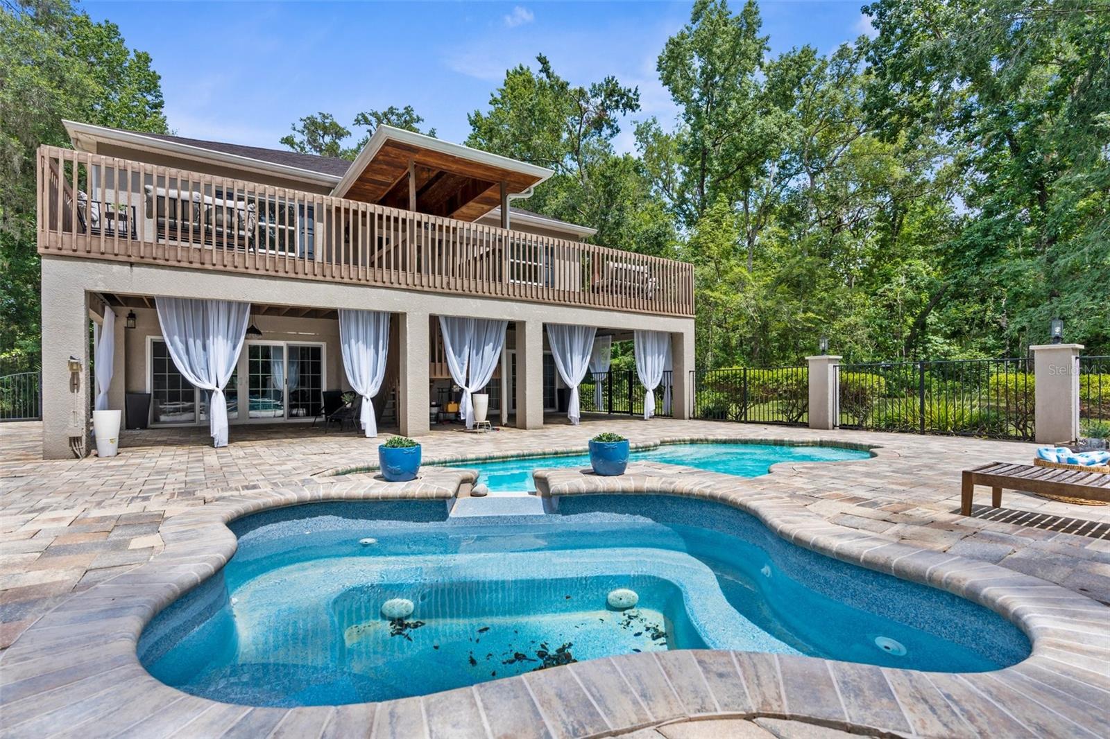 Heated pool and jacuzzi with paver deck and iron fence.