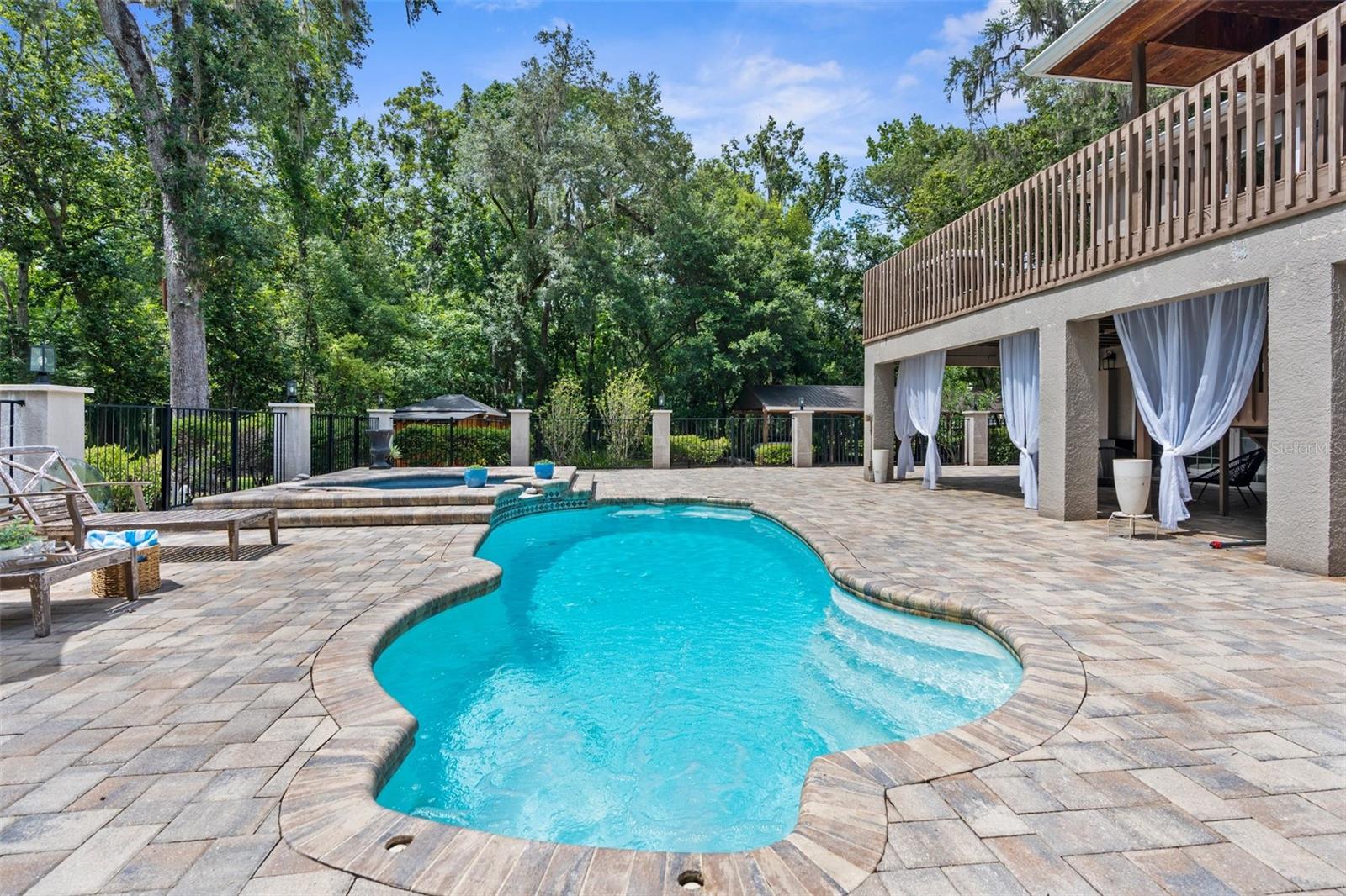 Heated pool and jacuzzi with paver deck and iron fence.