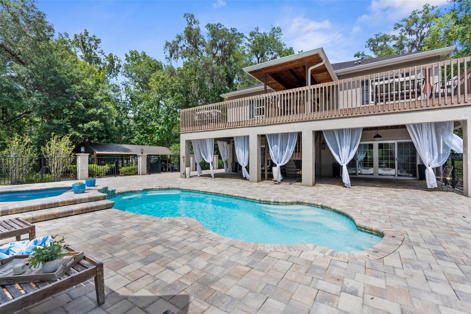 Heated pool and jacuzzi with paver deck and iron fence.