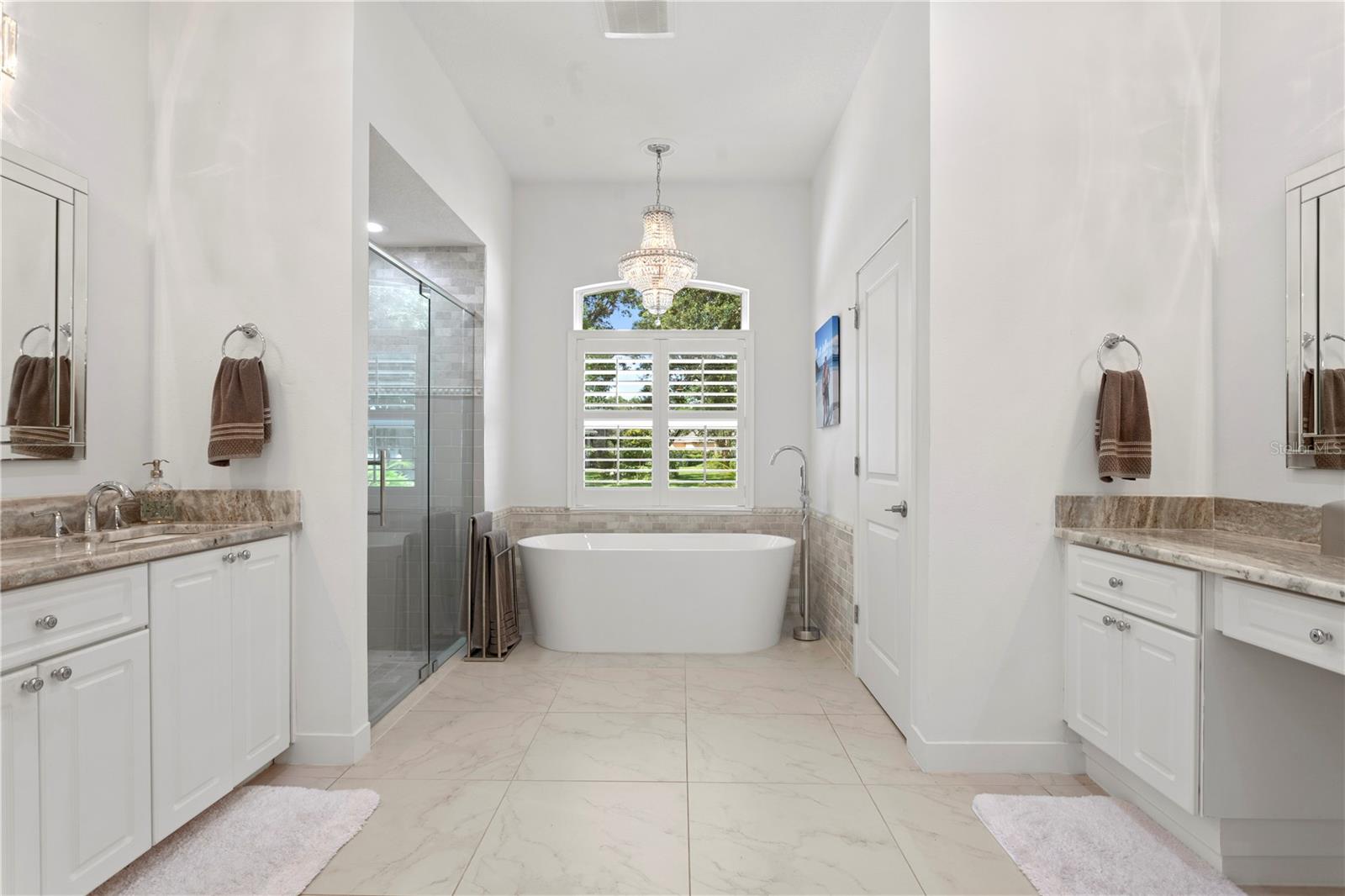 Unwind in style in the elegant soaking tub beneath a sparkling chandelier - the centerpiece of this spa-inspired en suite retreat.