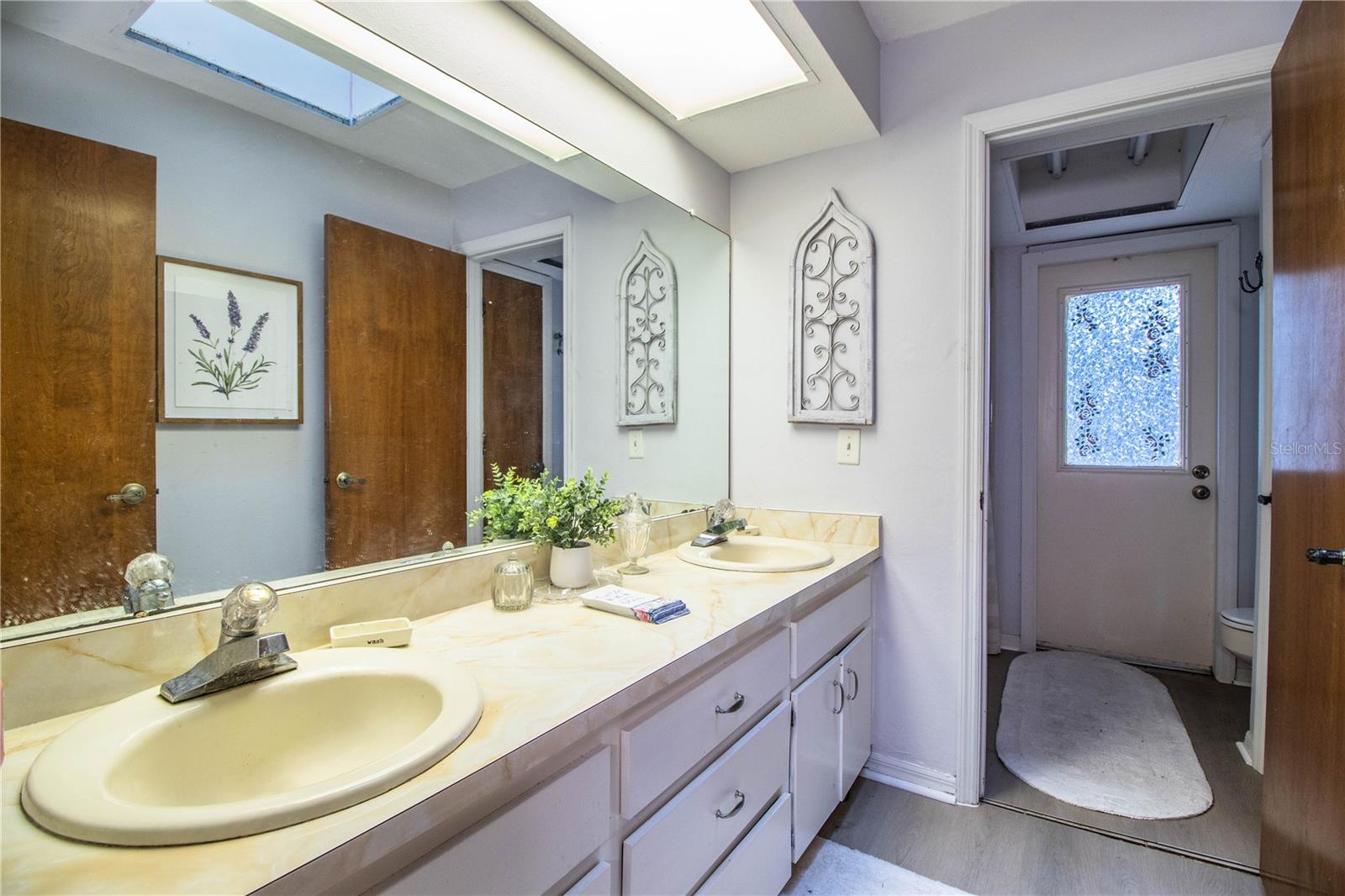 The guest bathroom includes a dual-sink vanity, oversized mirror, and stylish lighting, with a private shower and toilet area for added comfort.