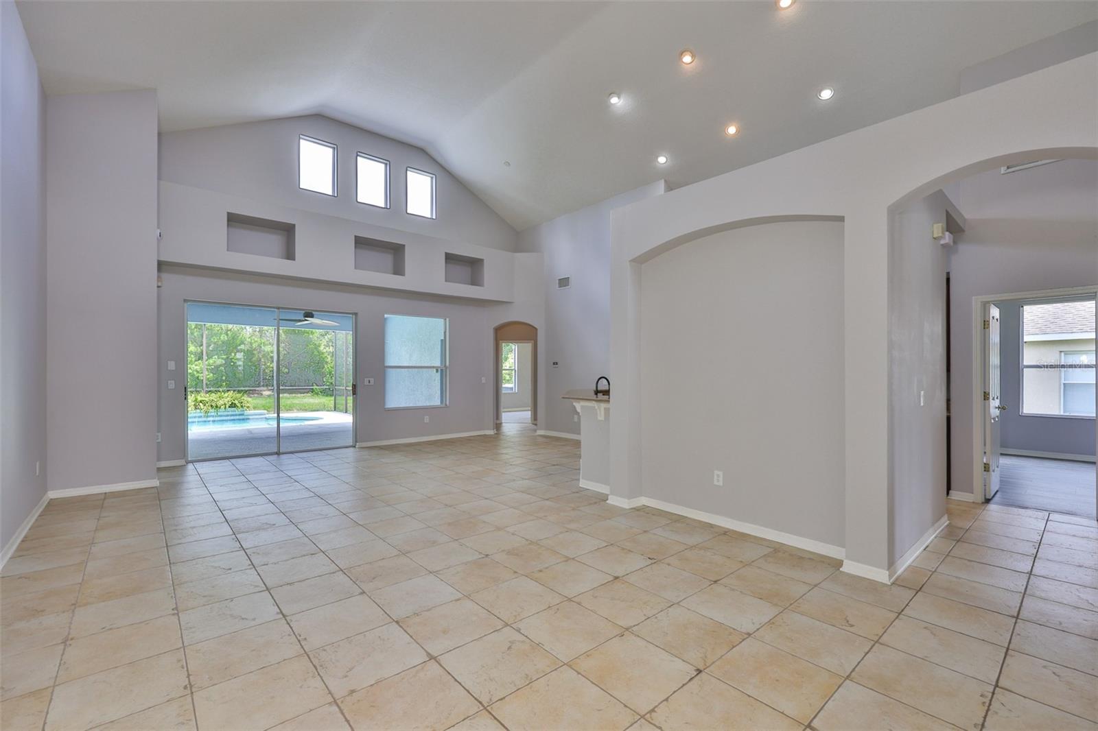 Great room with upper windows on opposite sides, sliders, lanai and pool, recessed lighting for kitchen