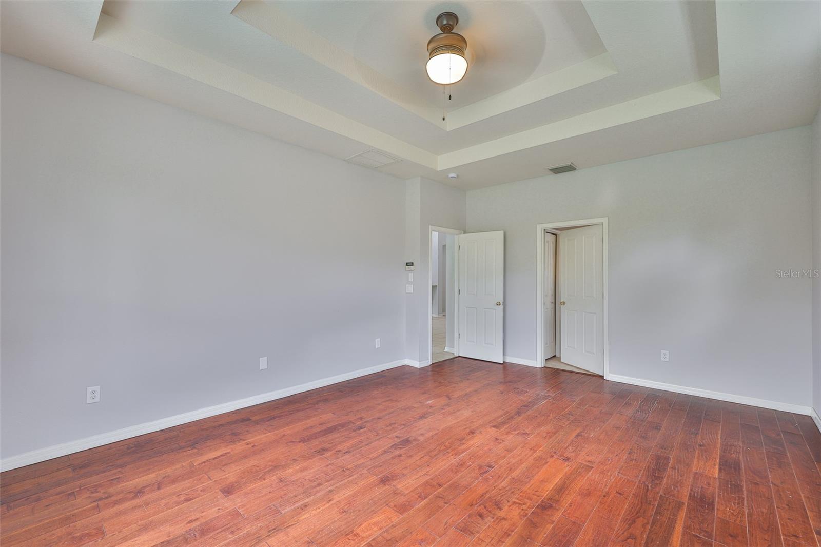 Primary bedroom suite with engineered hardwood, ceiling fan, double trey ceiling. Left open door to Great Room, center open door to en-suite bathroom and huge walk-in closet.