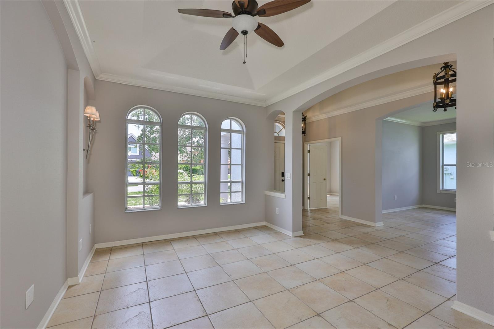 Formal dining room with ceiling fan, trey ceiling, window wall and wall sconces. View to rear - front door foyer, office and study/den