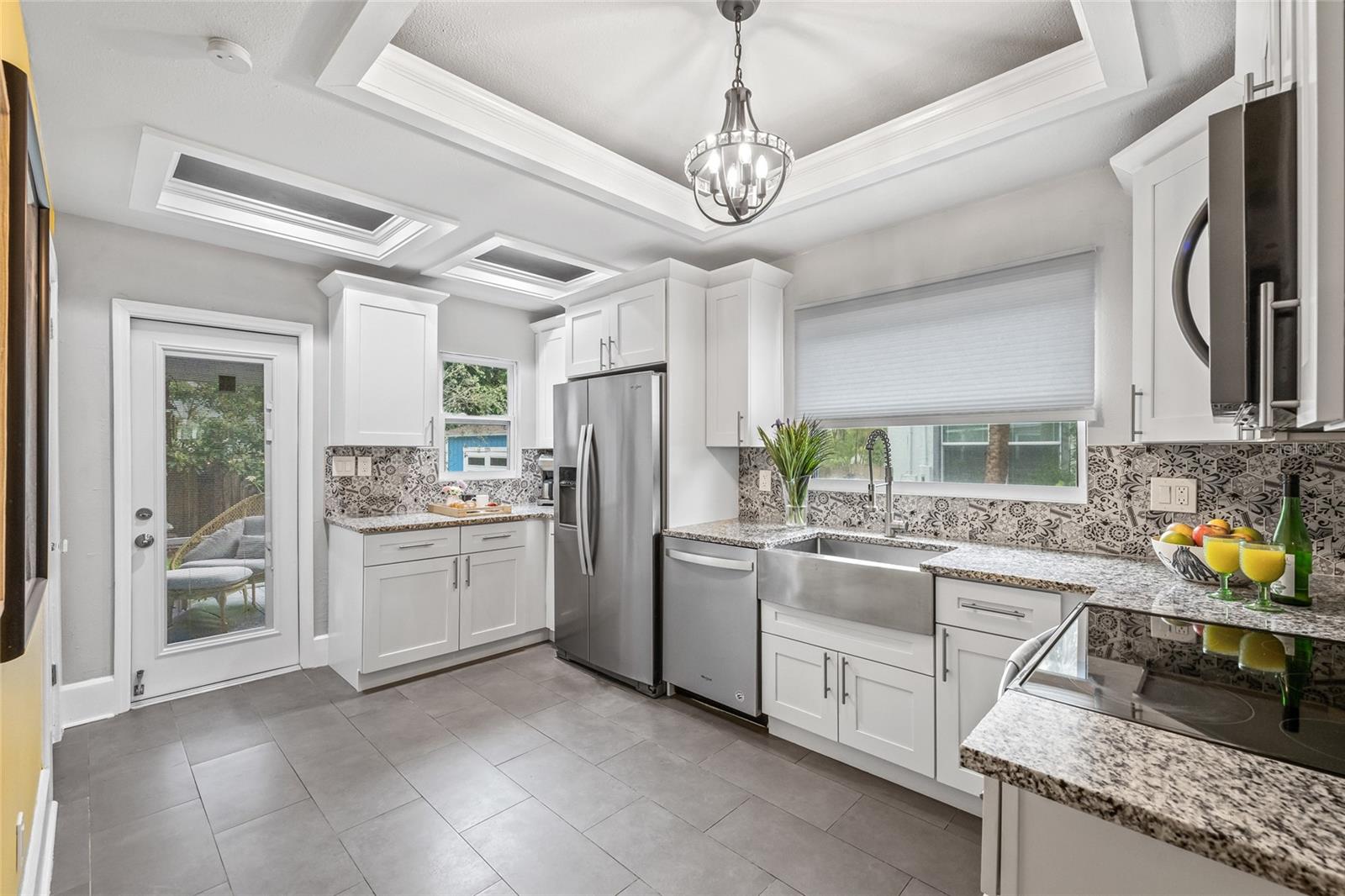 Crisp white cabinetry and elegant tray ceilings create a clean, contemporary space filled with natural light and convenient access to the backyard.