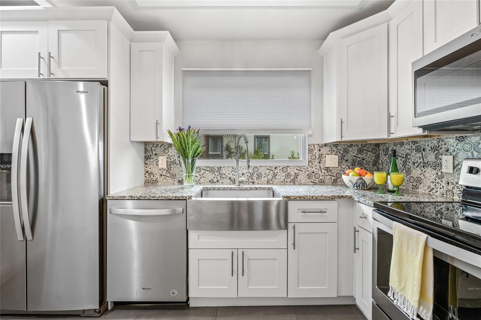 The oversized farmhouse sink is framed by a large window and accented by bold, designer tile backsplash.