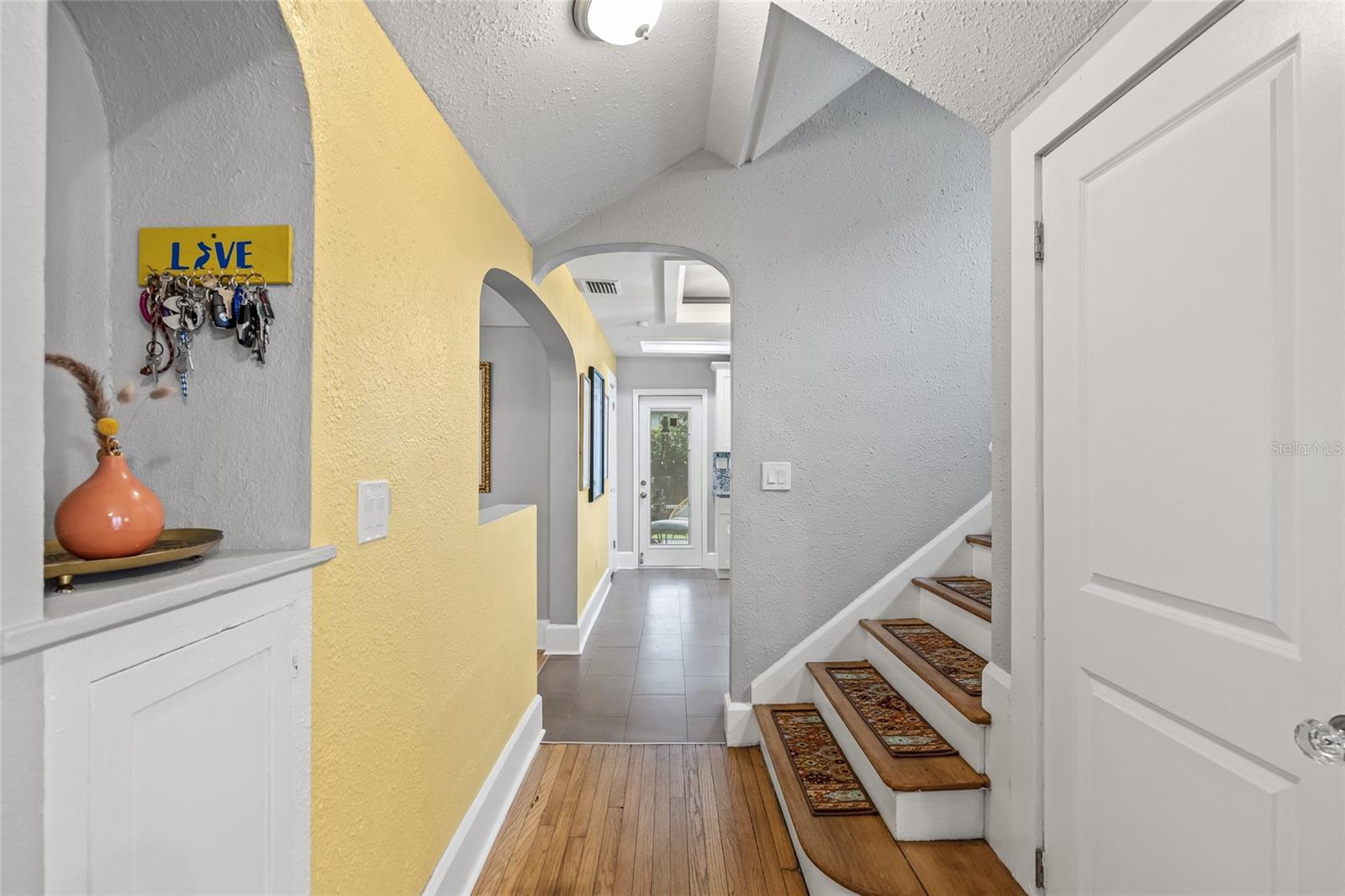 Inviting central hallway with original built in wall nook and cabinet, arched entryways, and access to kitchen, living areas, and upstairs bedrooms.