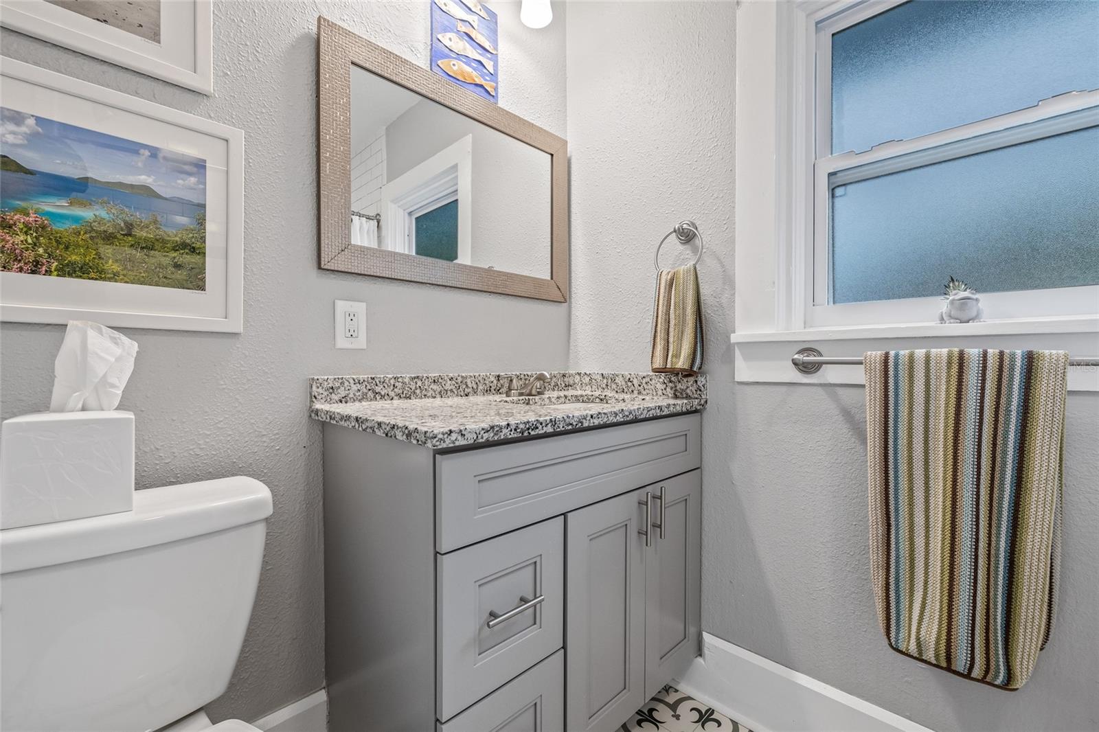 The shared bathroom also features a granite countertop, shaker-style cabinetry, and contemporary fixtures with plenty of storage.