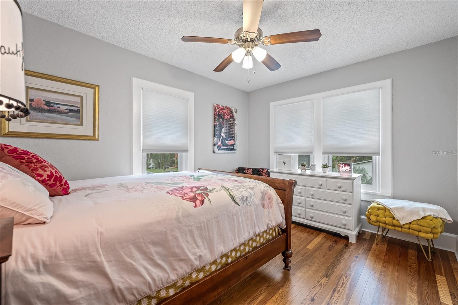 Bedroom 3, surrounded by windows, this serene space offers natural light, ceiling fan, and more of the gorgeous hardwood floors.