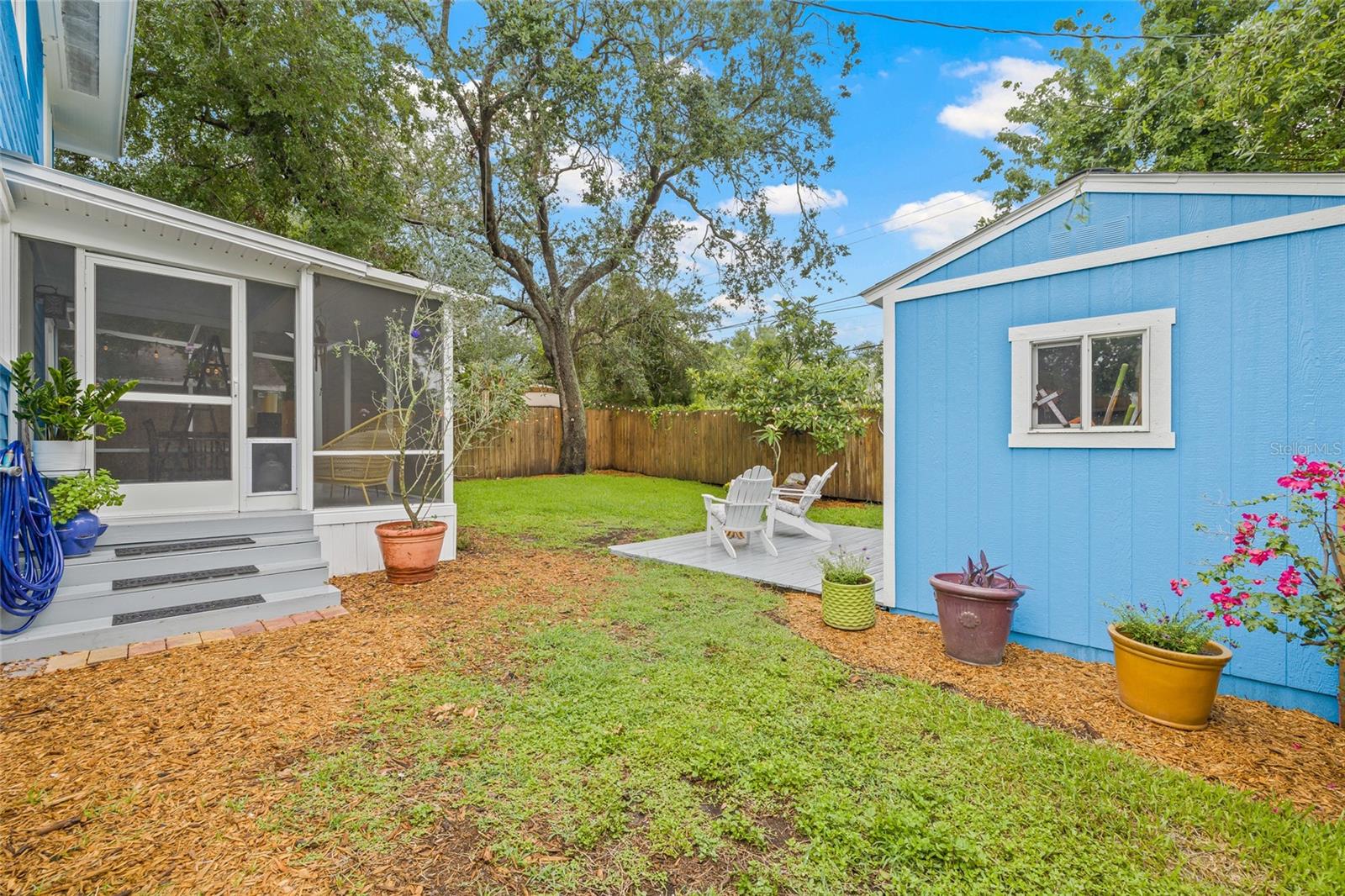 Spacious fenced backyard with multipurpose deck, perfect for lounging, entertaining, or enjoying cozy evenings under the trees.